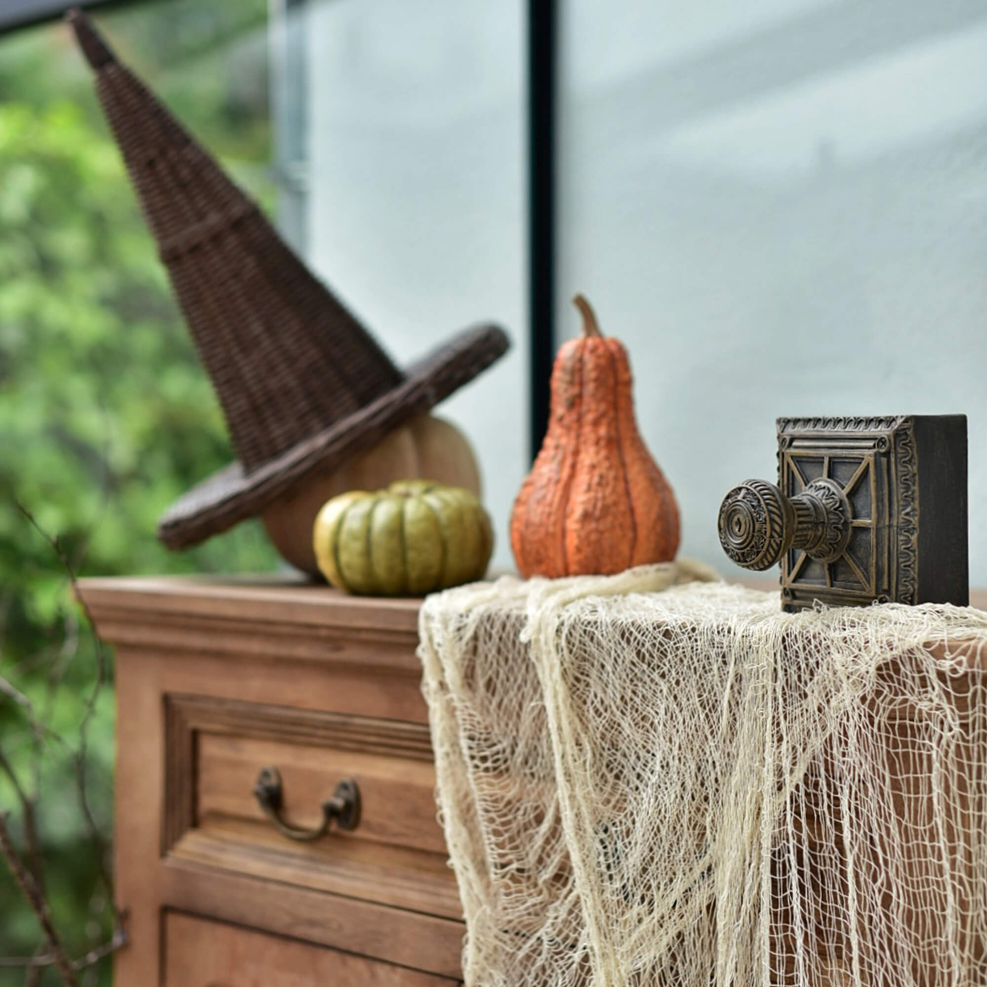 Comò in legno con cappello da strega in vimini e zucche per decorazioni di Halloween