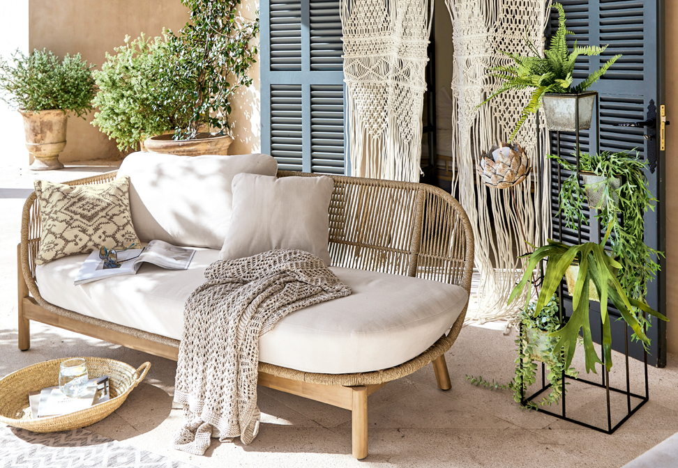 Divano boho con rivestimento beige chiaro e struttura in legno, decorato con cuscini e coperta lavorata