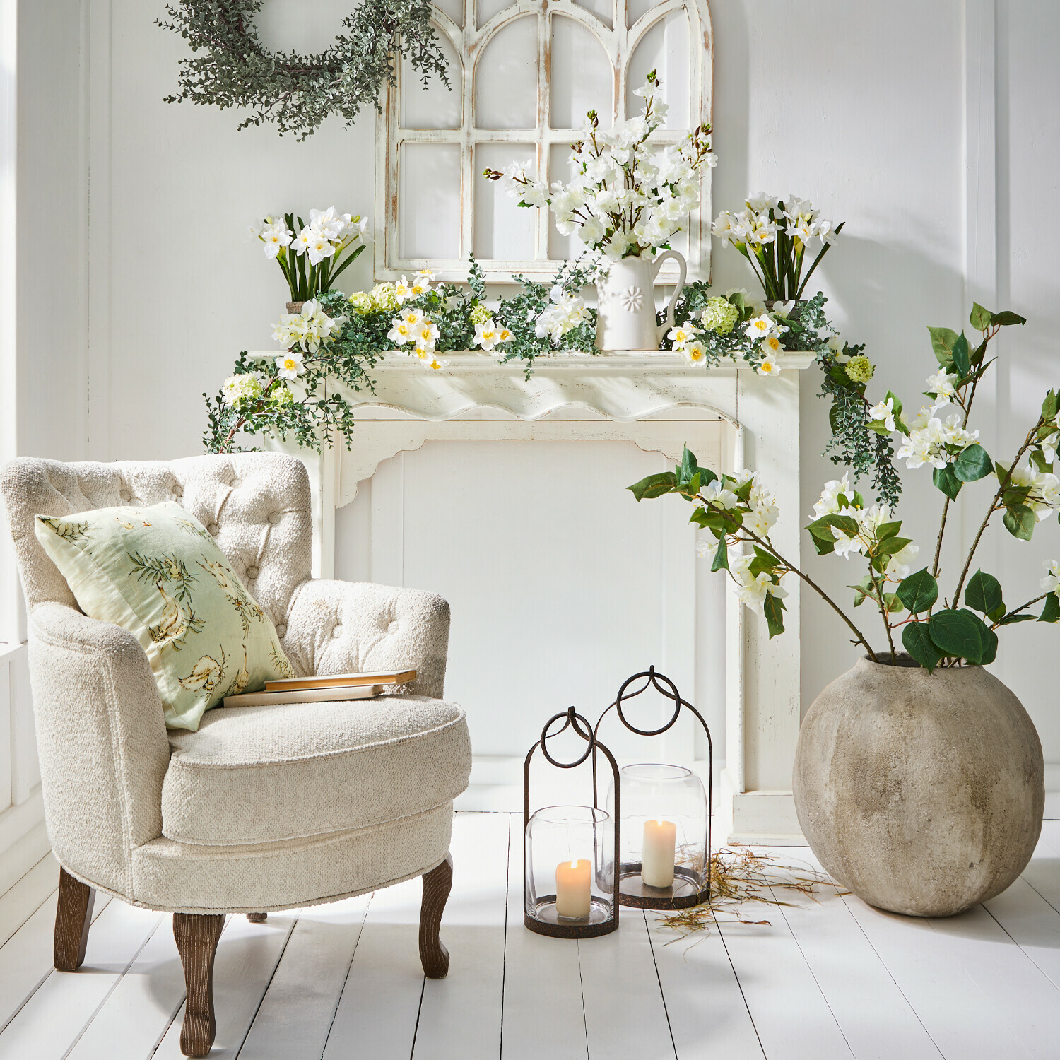 Consolle caminetto Claybourne Poltrona crema confortevole con gambe in legno accanto a camino decorativo con fiori bianchi e candele