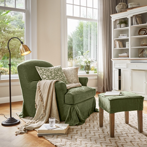 Poltrona verde in tessuto con poggiapiedi e coperta beige in soggiorno luminoso con grande finestra
