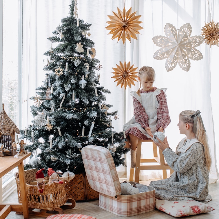 Bambini accanto a un albero di Natale decorato con ornamenti naturali e stelle di carta in una stanza luminosa