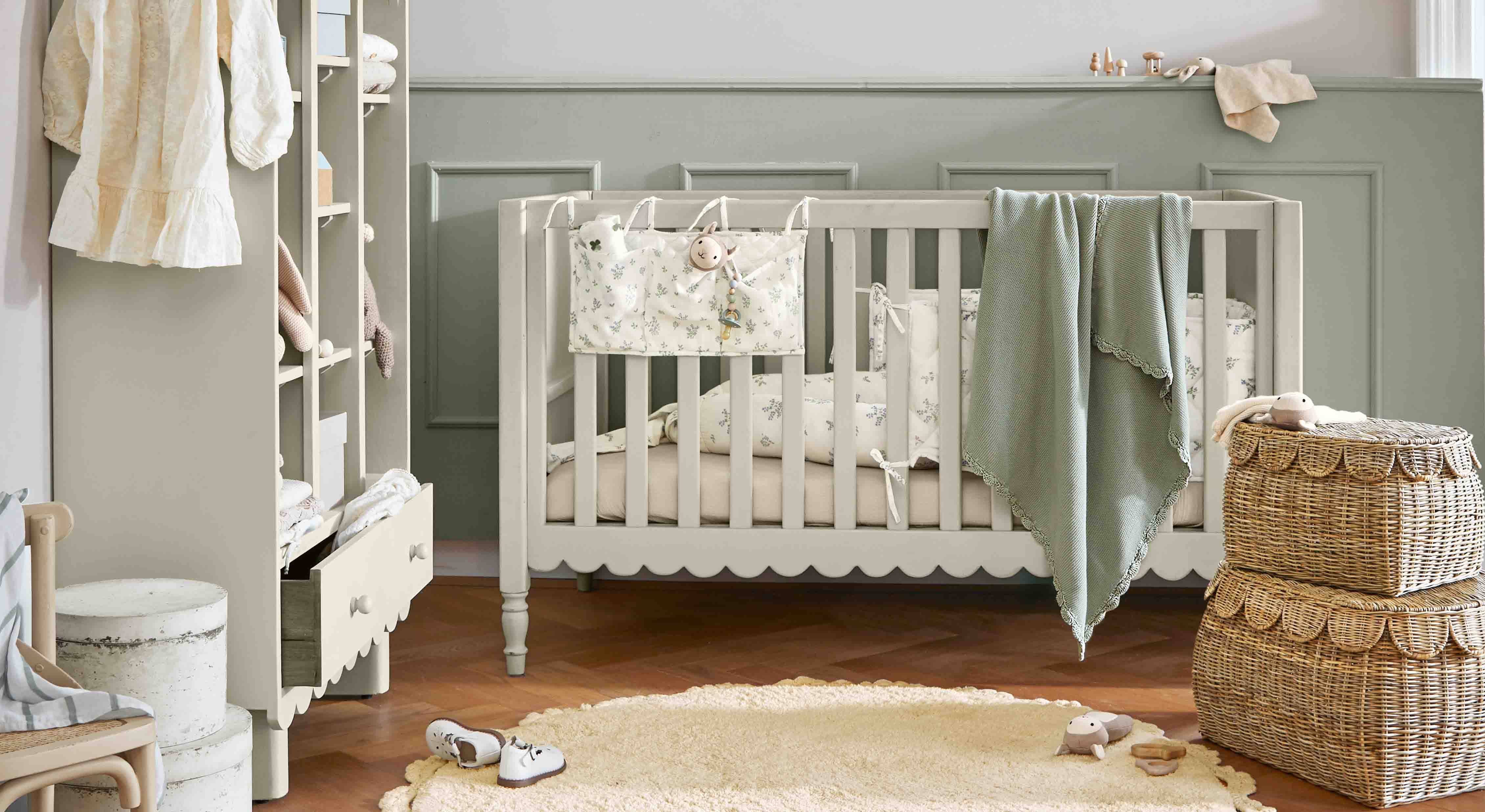 Lettino per bambini in legno grigio con coperta verde e cesti in vimini in una cameretta accogliente