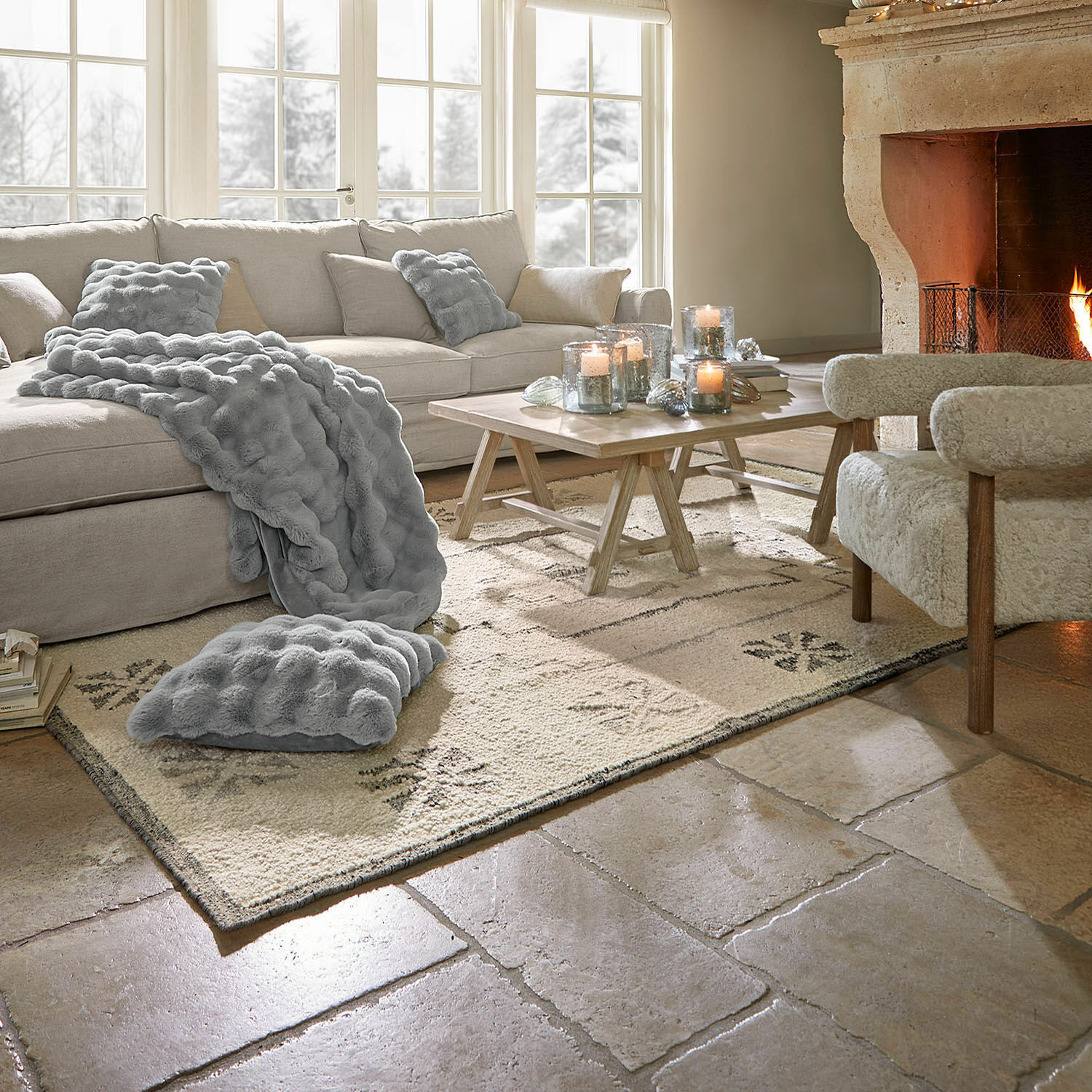 Tappeto Xerven Soggiorno accogliente con divano beige, coperta e cuscini grigi, camino acceso e tavolino in legno