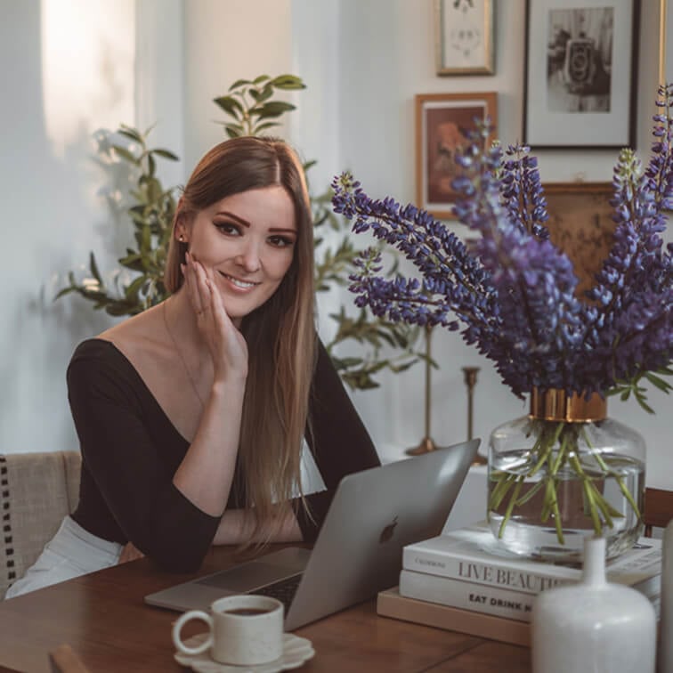 Donna che lavora al laptop su tavolo in legno con mazzo di fiori viola e tazza di caffè