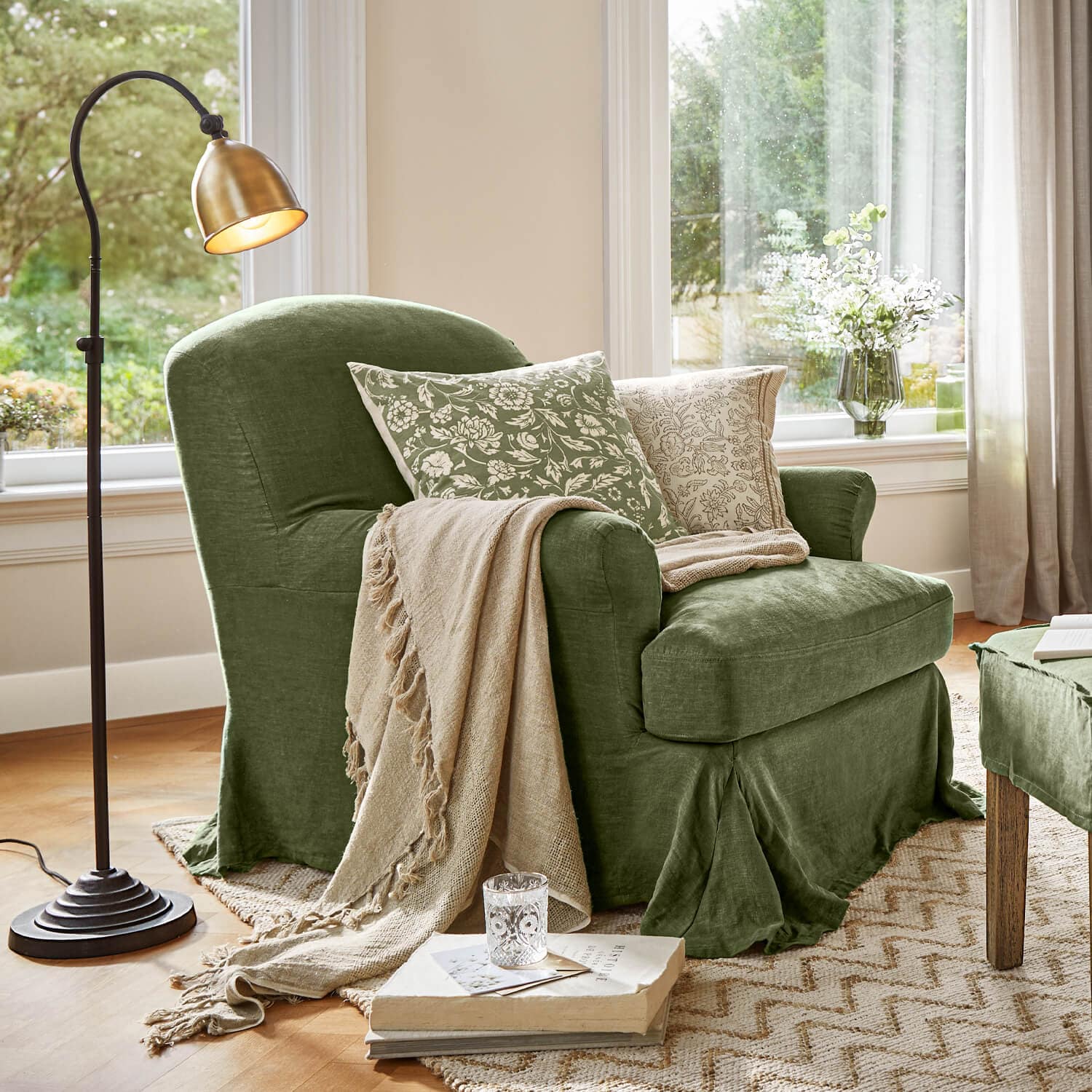 Poltrona verde in tessuto con coperta beige e cuscini floreali in soggiorno luminoso