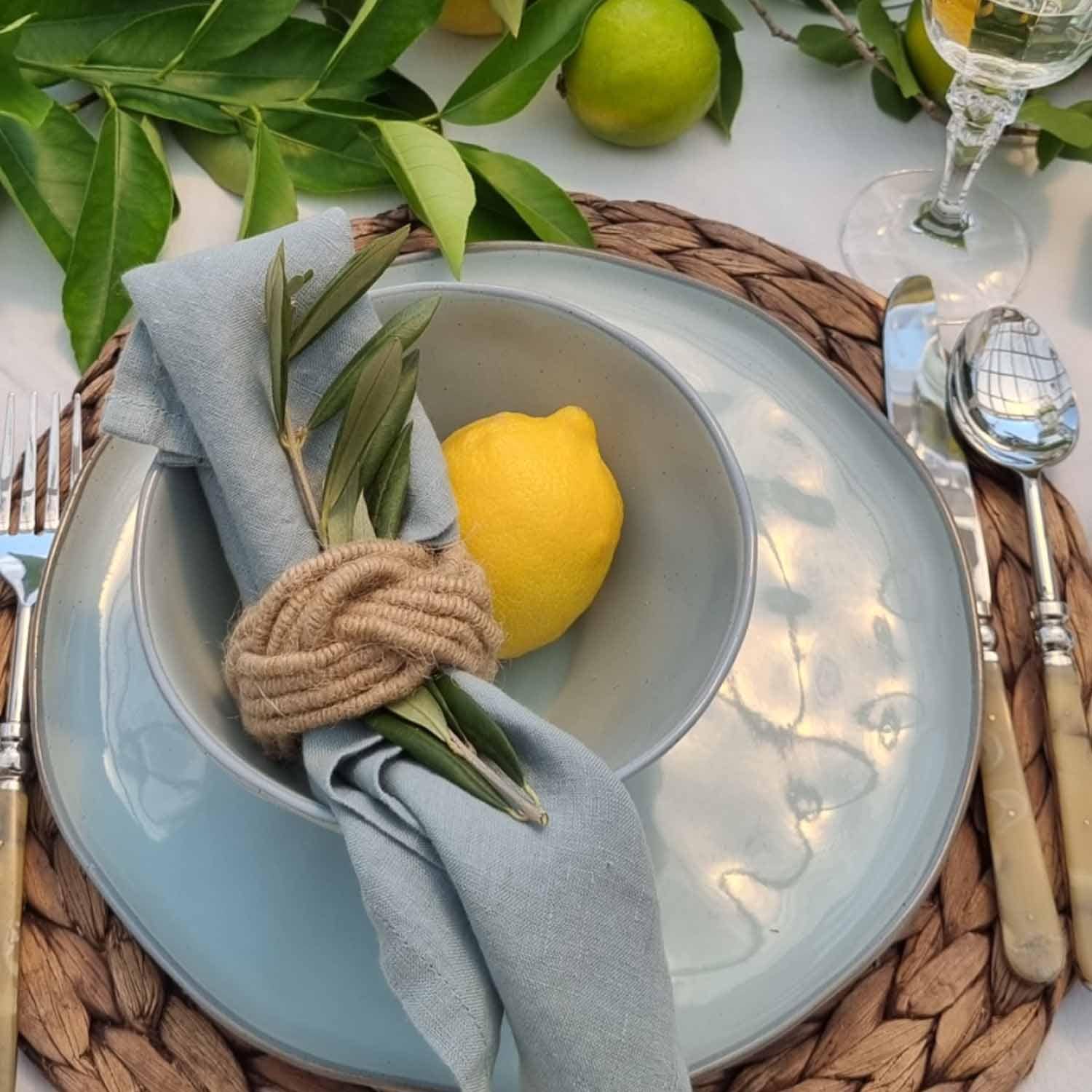 Servizio da tavola in ceramica blu con tovagliolo di lino e limone su sottopiatto in vimini