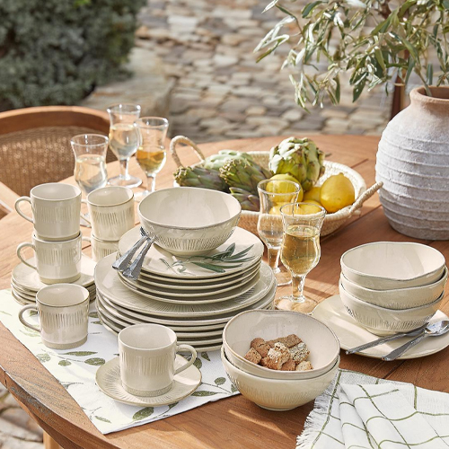 Set di stoviglie in ceramica crema con motivo di foglie verdi su tavolo in legno all'aperto
