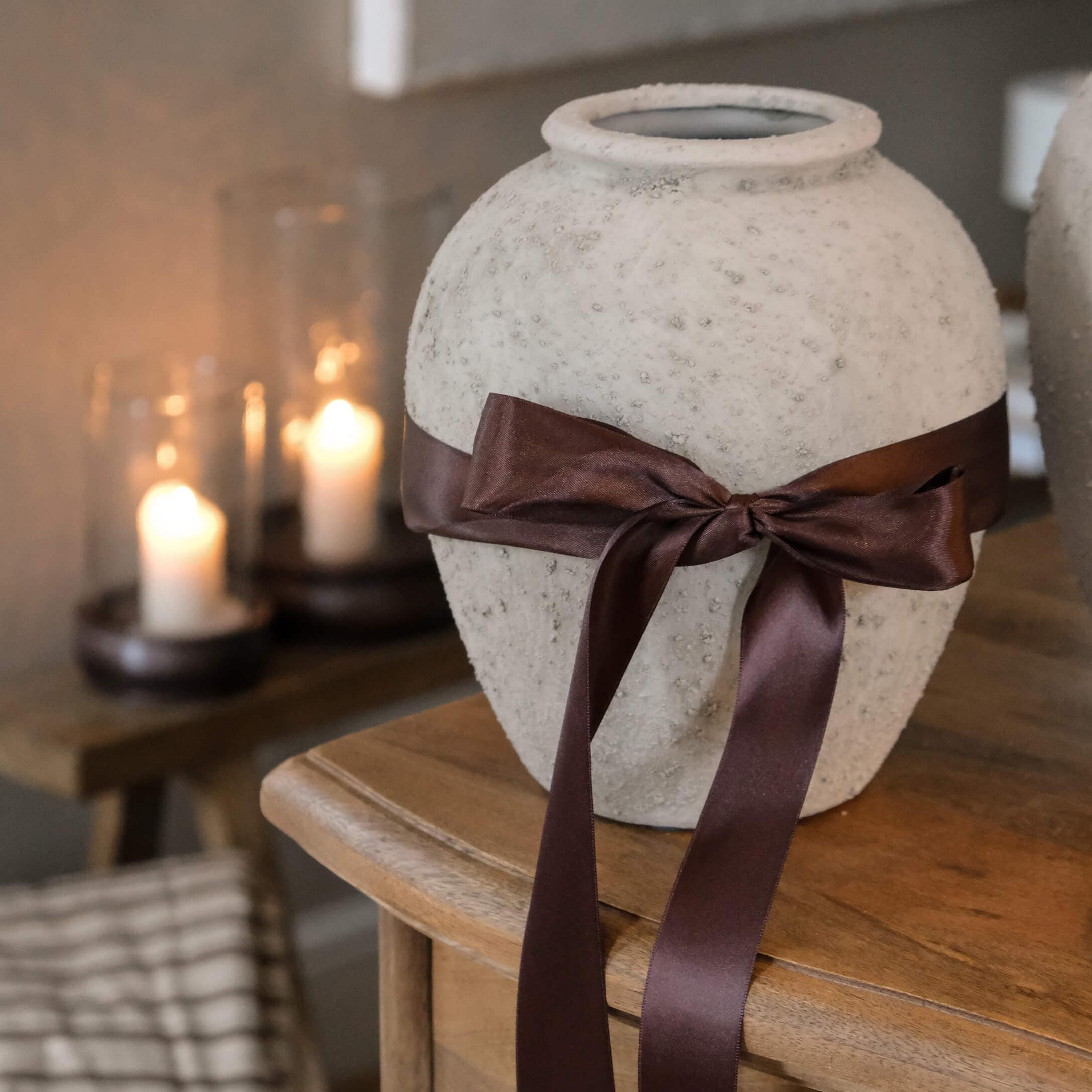 Vaso decorativo bianco con texture e fiocco di raso marrone su tavolo in legno in ambiente accogliente