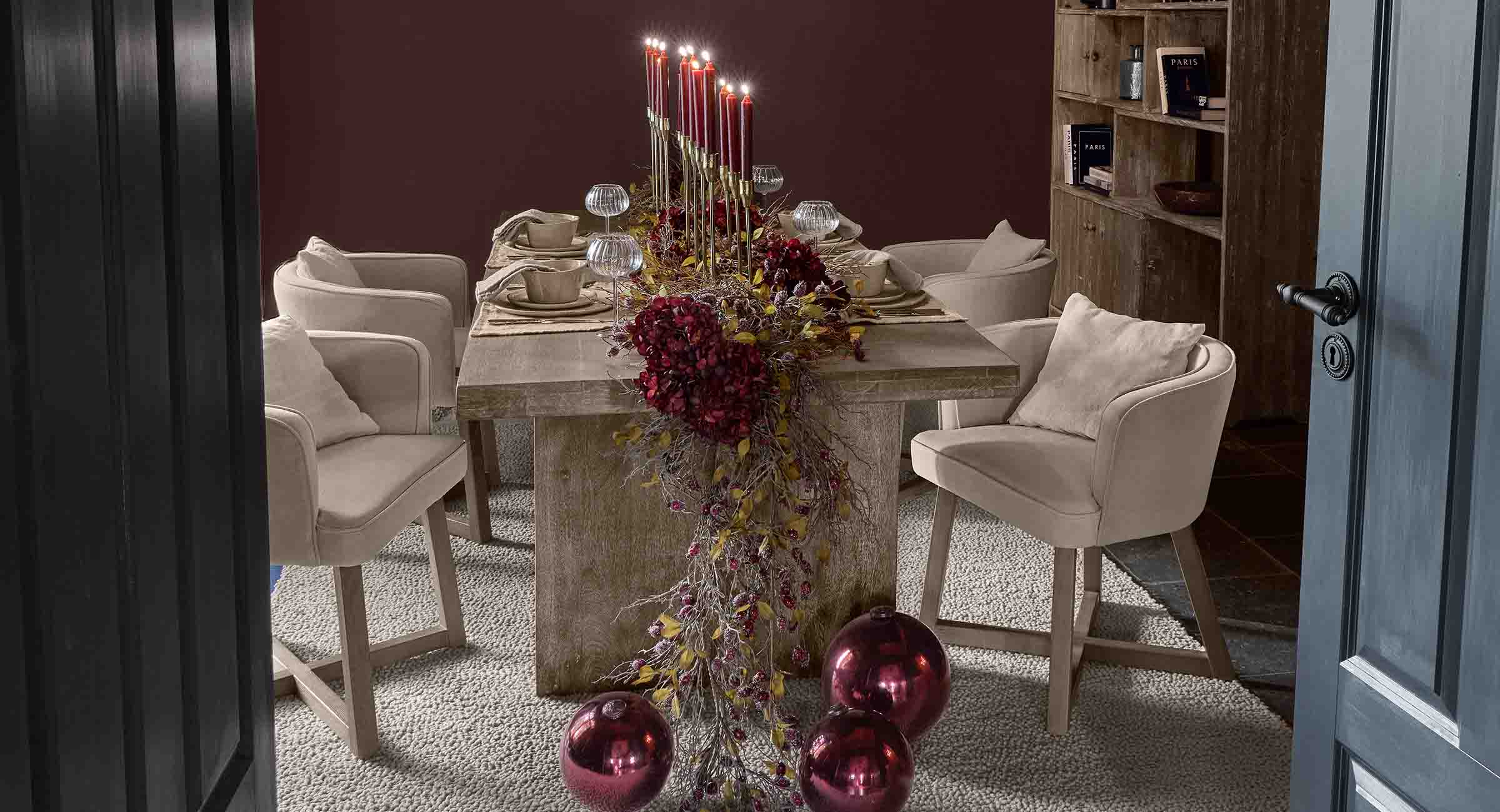Tavolo da pranzo elegante con sedie beige e decorazioni festive rosse con candele accese