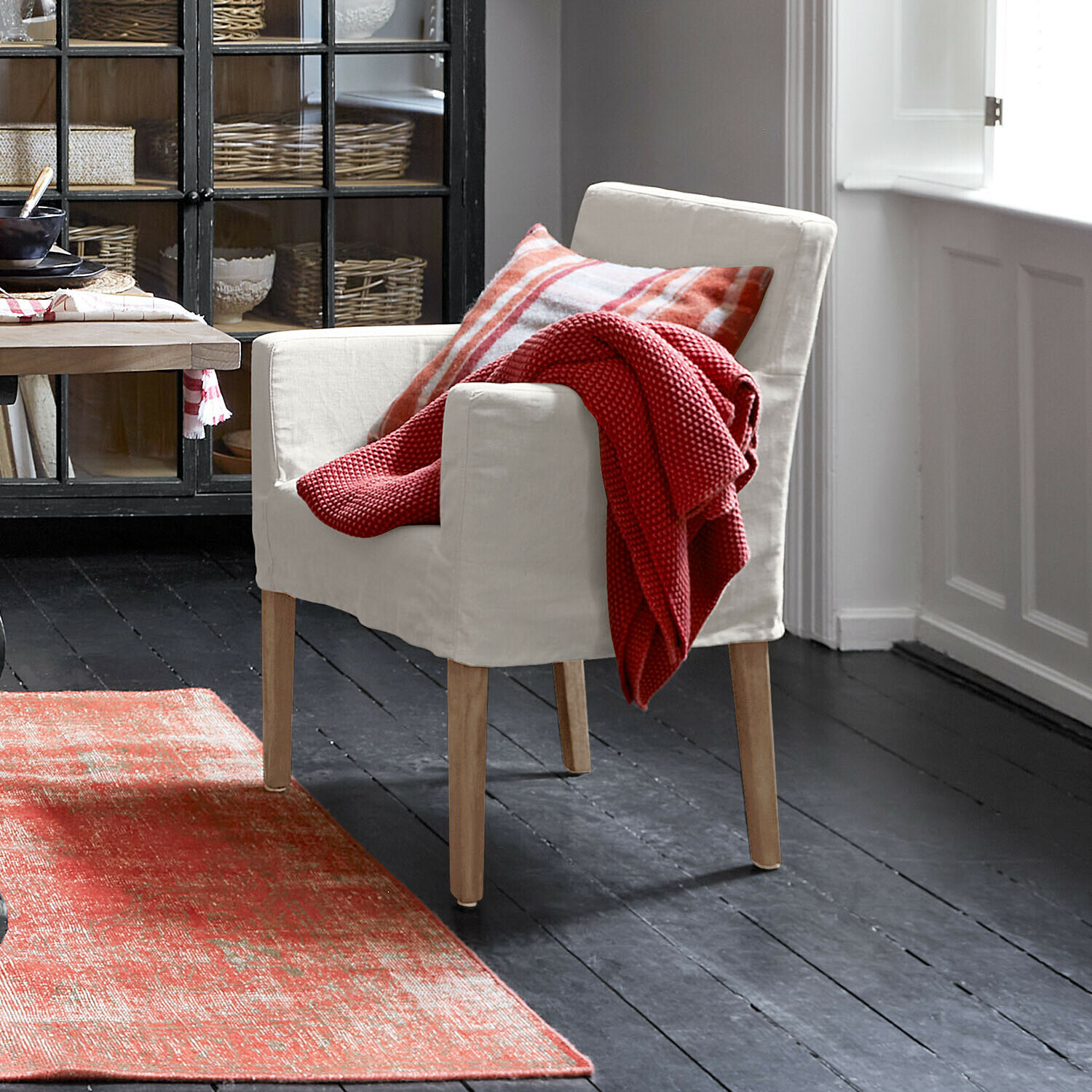 Sedia Longhill Poltrona beige con gambe in legno, coperta rossa e cuscino a quadri in ambiente accogliente