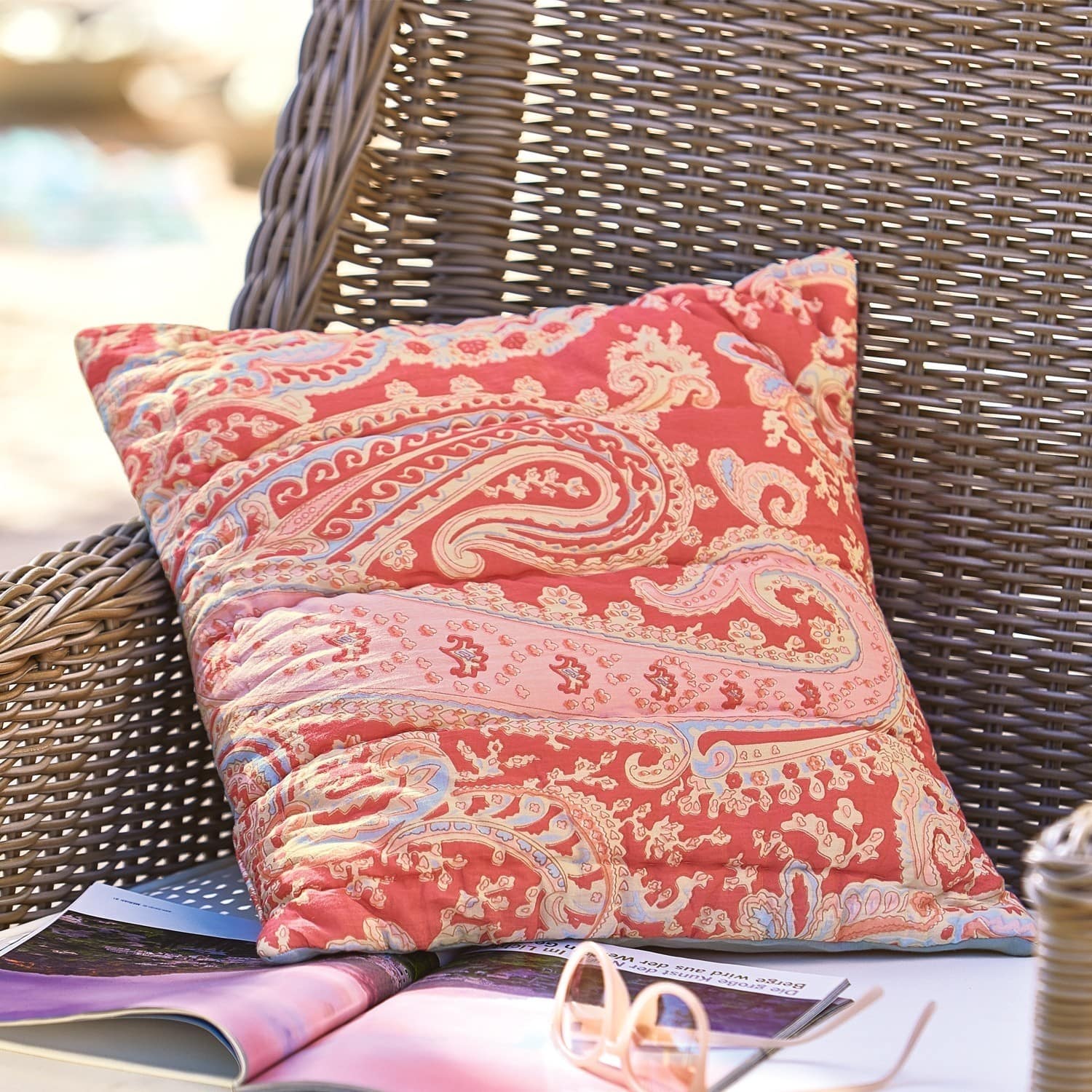 Copricuscino Aram Cuscino decorativo in cotone rosso con motivo paisley su poltrona in vimini all'aperto