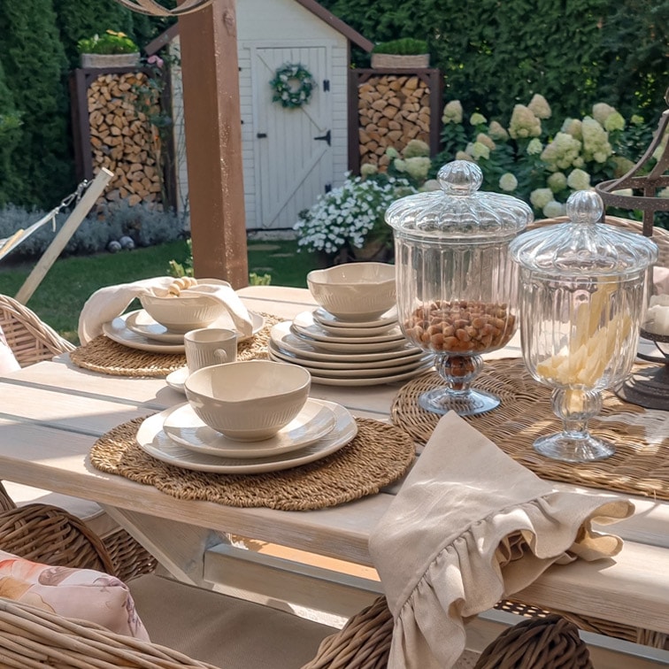 Servizio di ceramica bianca su tavolo in legno chiaro con barattoli di vetro decorativi in giardino