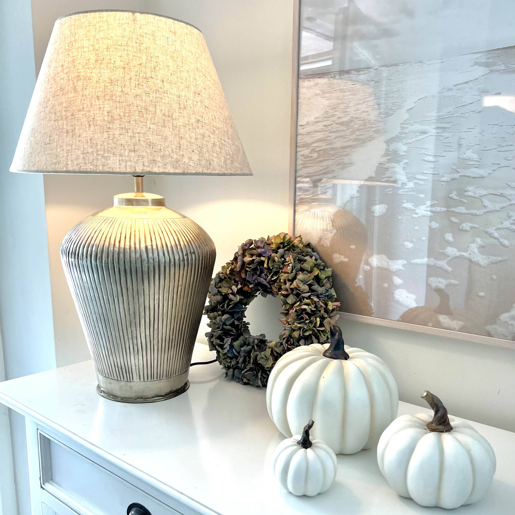 Lampada da tavolo con paralume beige e base in ceramica, zucche bianche decorative e corona di fiori secchi