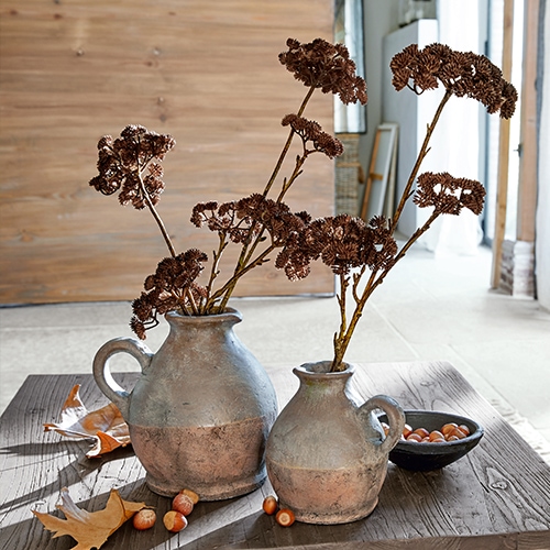 Due brocche in ceramica grigio-marrone con fiori secchi su tavolo di legno con nocciole