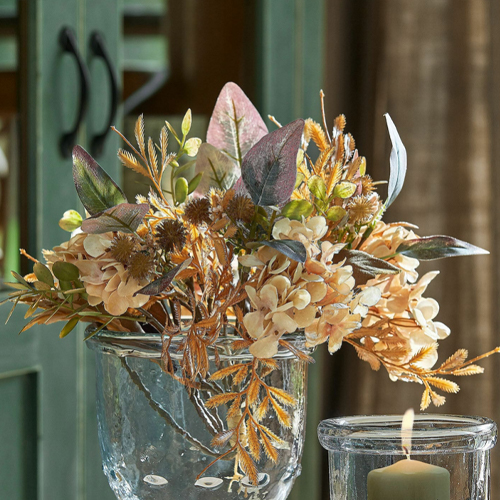 Composizione decorativa di fiori artificiali in vaso di vetro davanti a porta verde e candela