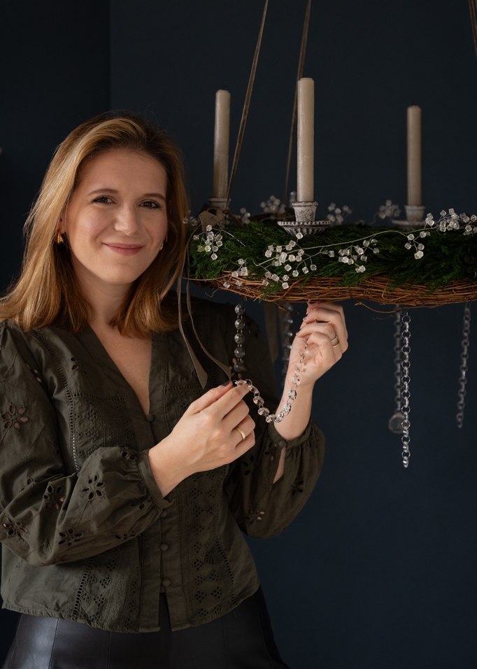 Donna che decora corona d'Avvento verde con candele bianche e ornamenti di cristallo su sfondo scuro