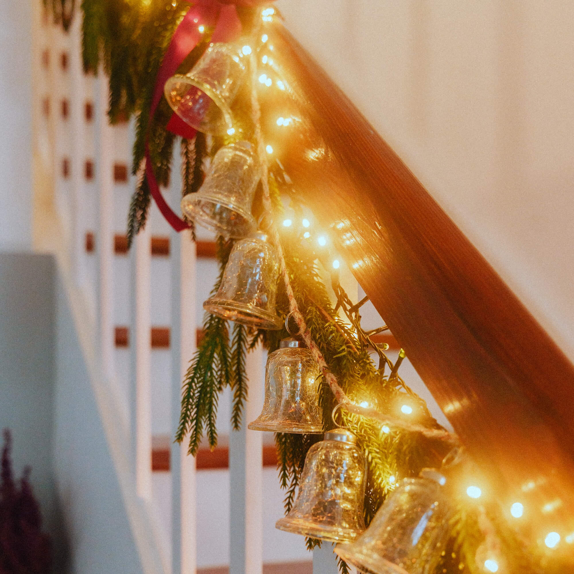 Campanelle di vetro e luci LED su corrimano in legno con rami verdi decorazione natalizia