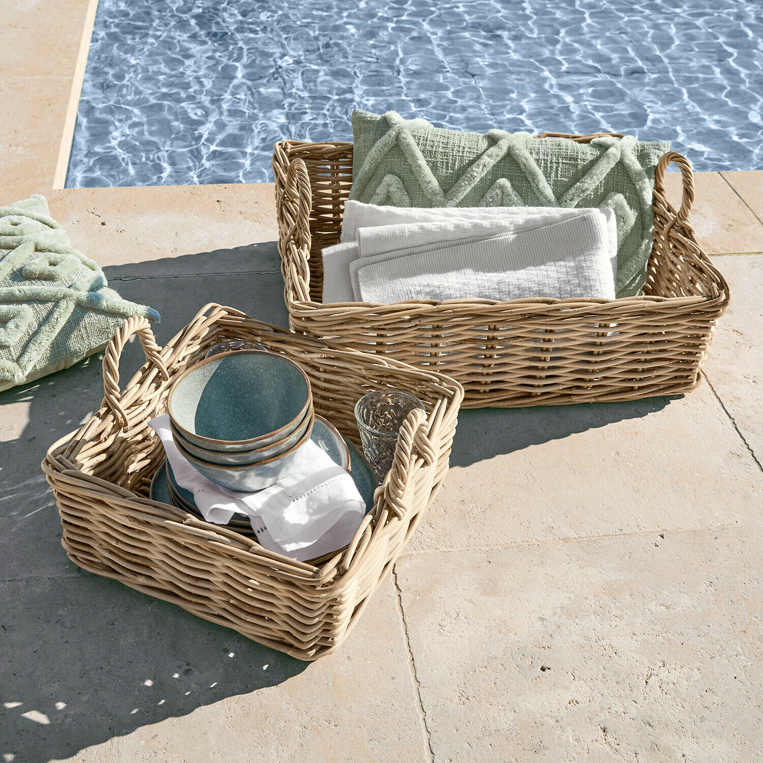 Due ceste di vimini con manici, riempite con cuscini verdi e asciugamani bianchi vicino alla piscina