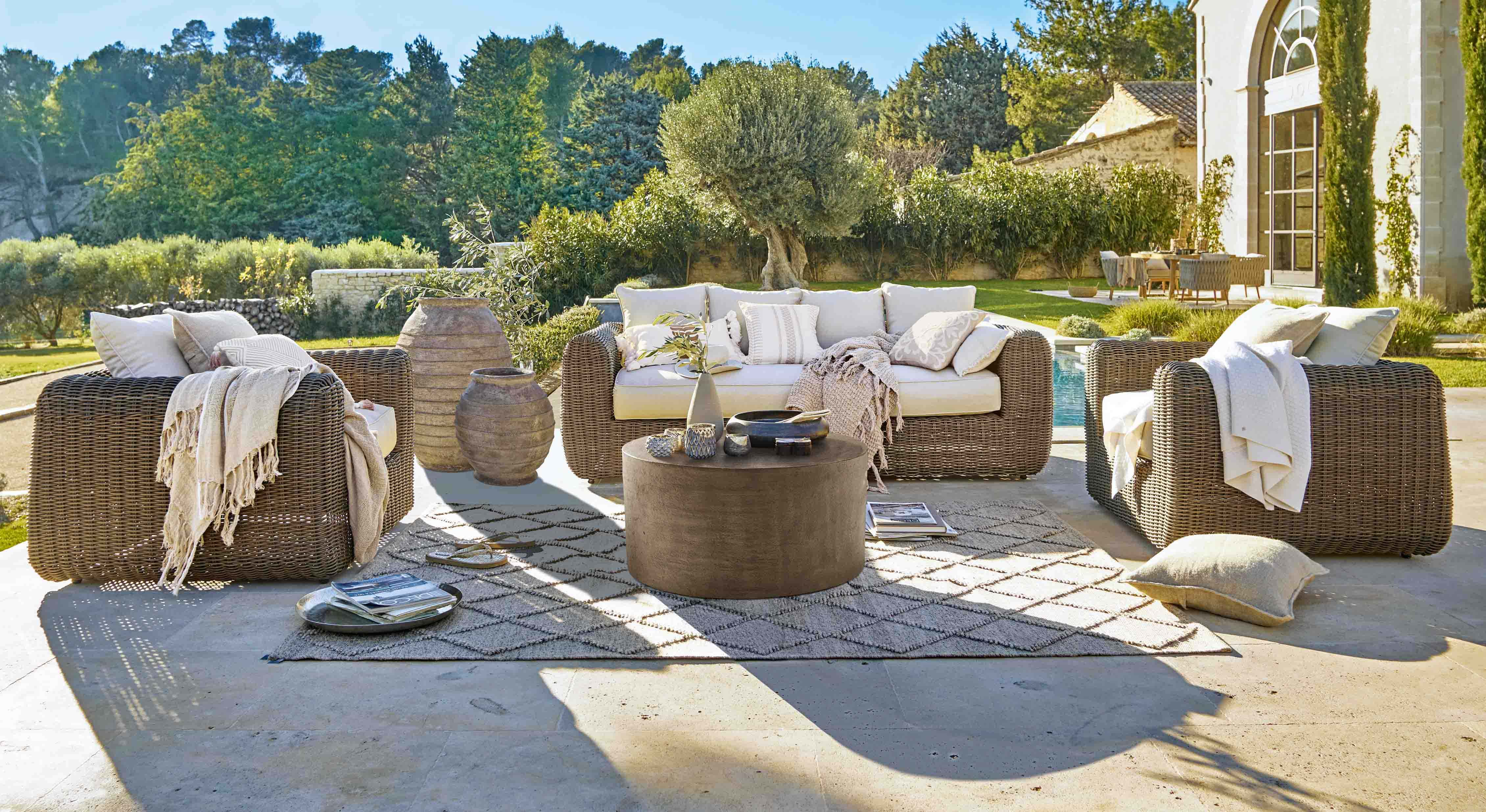 Set di mobili da giardino in rattan marrone con cuscini crema e tavolino rotondo su terrazza soleggiata