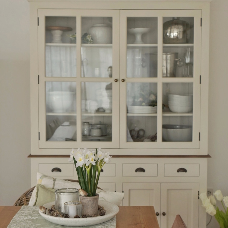 Vetrina in legno color crema con ante in vetro e decorazione da tavolo con fiori e candele