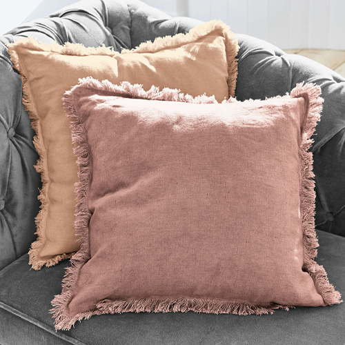 Due cuscini decorativi in lino rosa e beige con frange su divano grigio, atmosfera accogliente