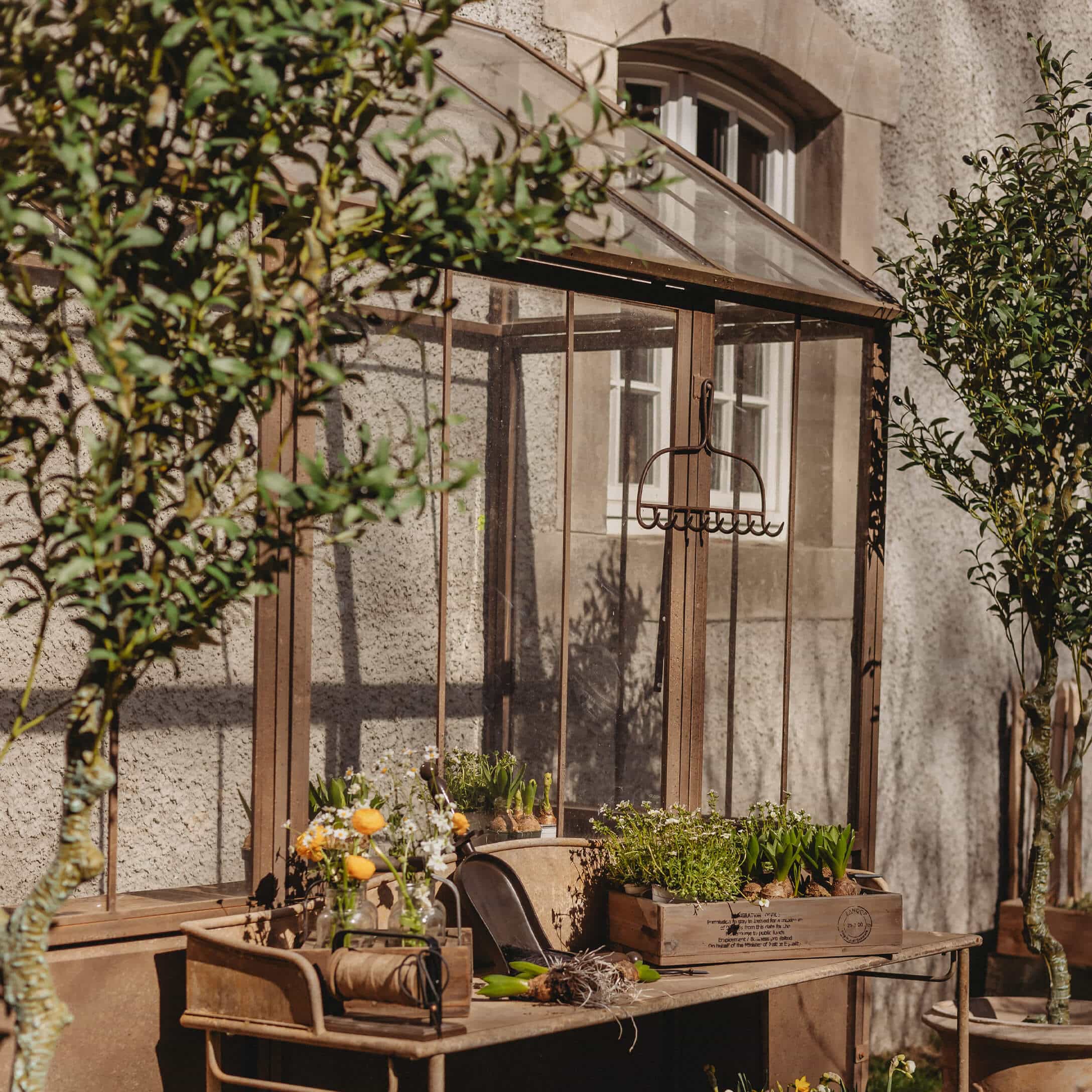Tavolo da giardino in metallo vintage con vasi e attrezzi davanti a una serra di vetro