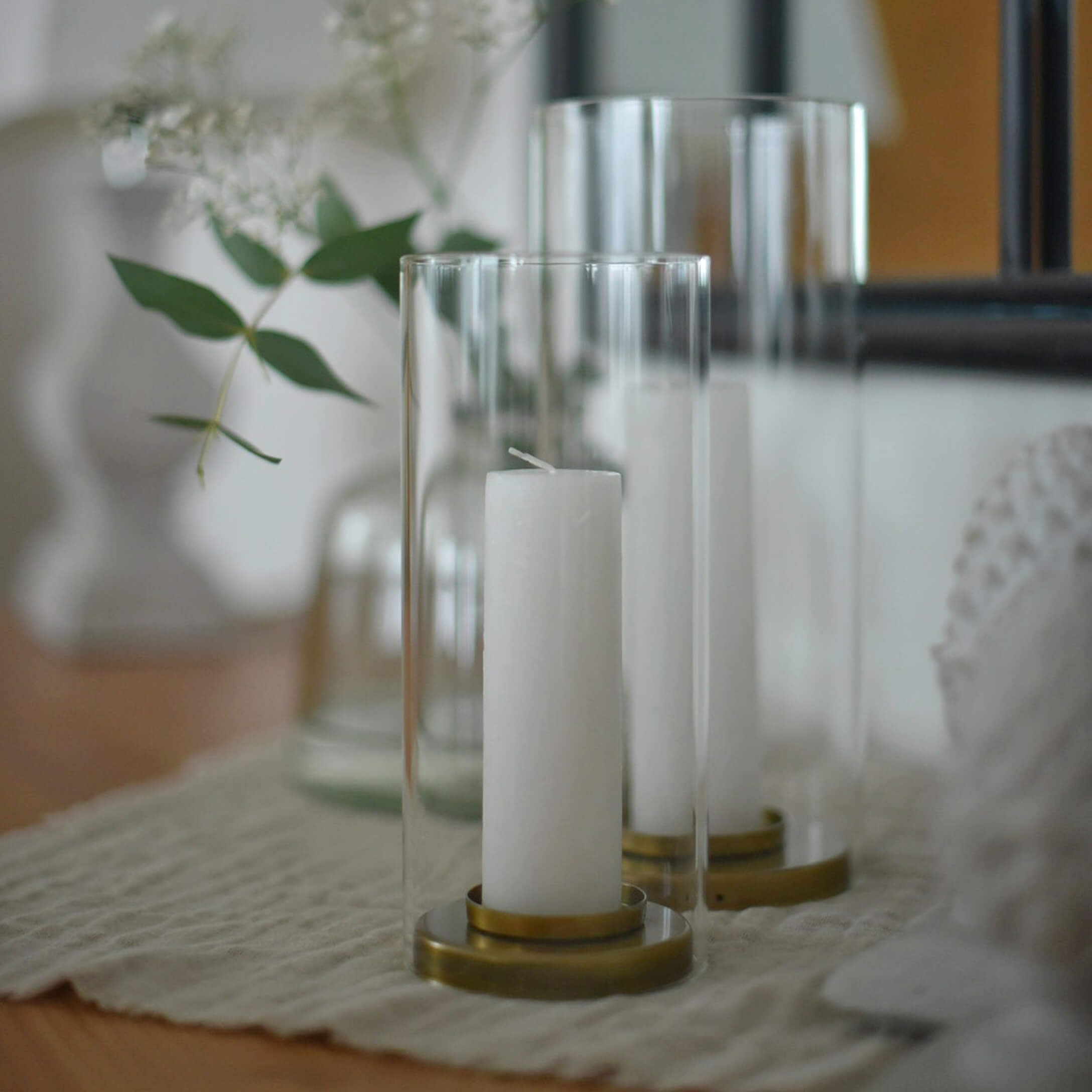 Candele bianche in lanterne di vetro trasparente con base in ottone su tovaglia beige