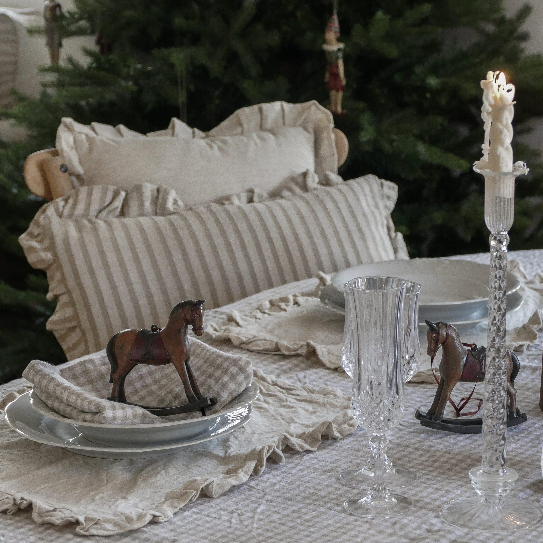 Tavolo rustico con tovaglia di lino beige a righe, cuscini coordinati e decorazioni a cavalluccio a dondolo in legno