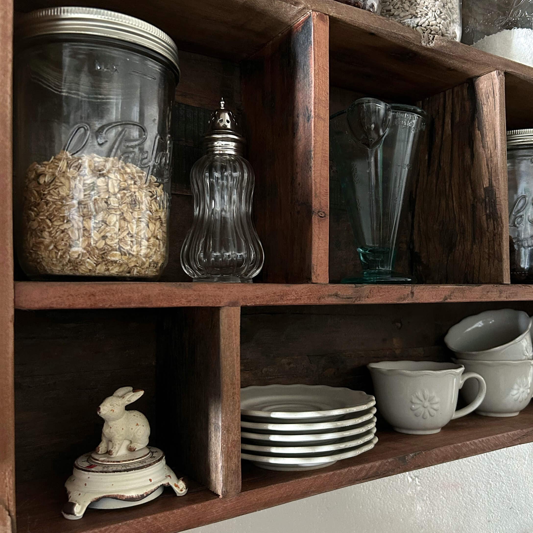 Mensola in legno con barattoli di vetro trasparente e stoviglie bianche in ceramica