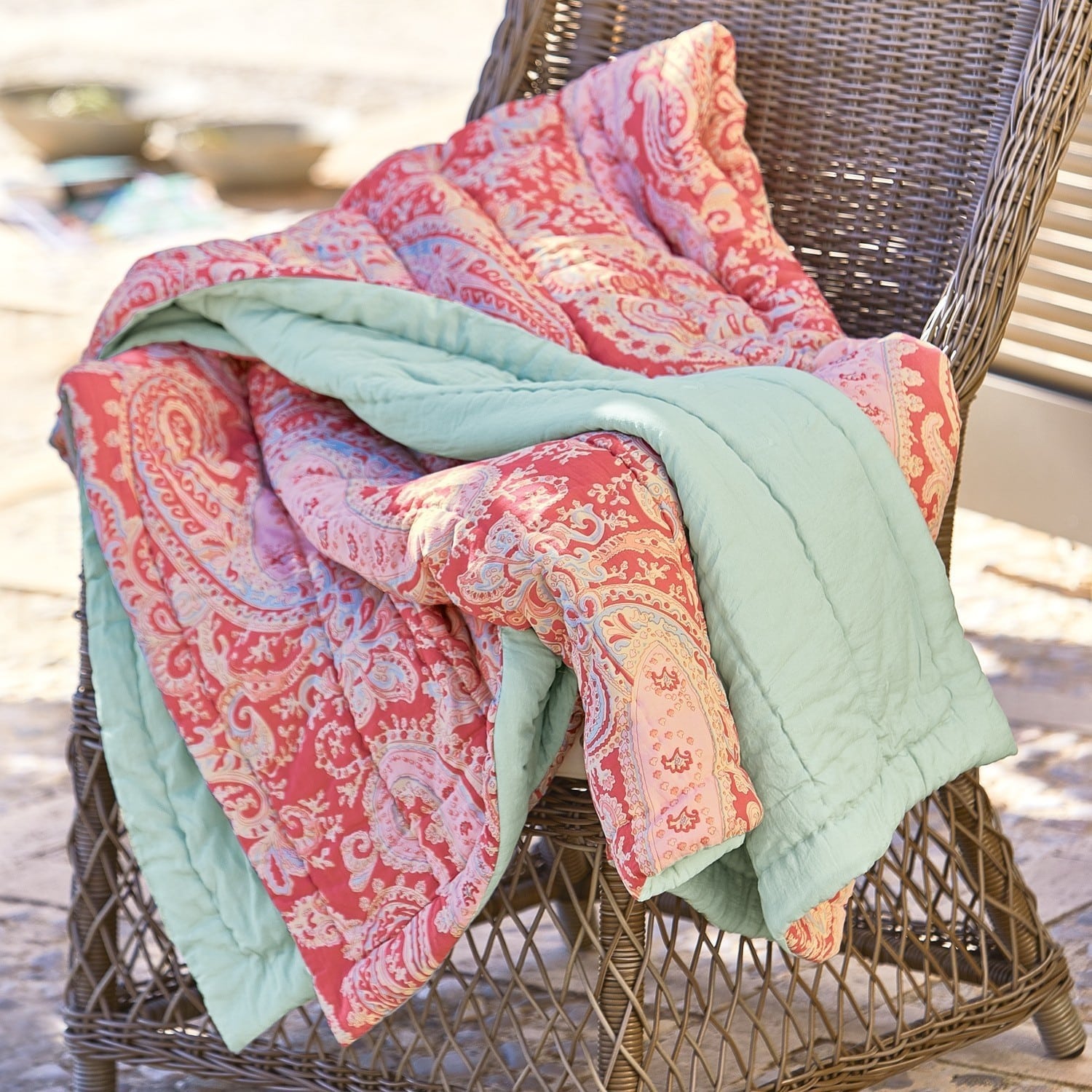 Coperta trapuntata Aram Coperta reversibile con motivo paisley rosso e rosa e fodera verde morbida su sedia in vimini