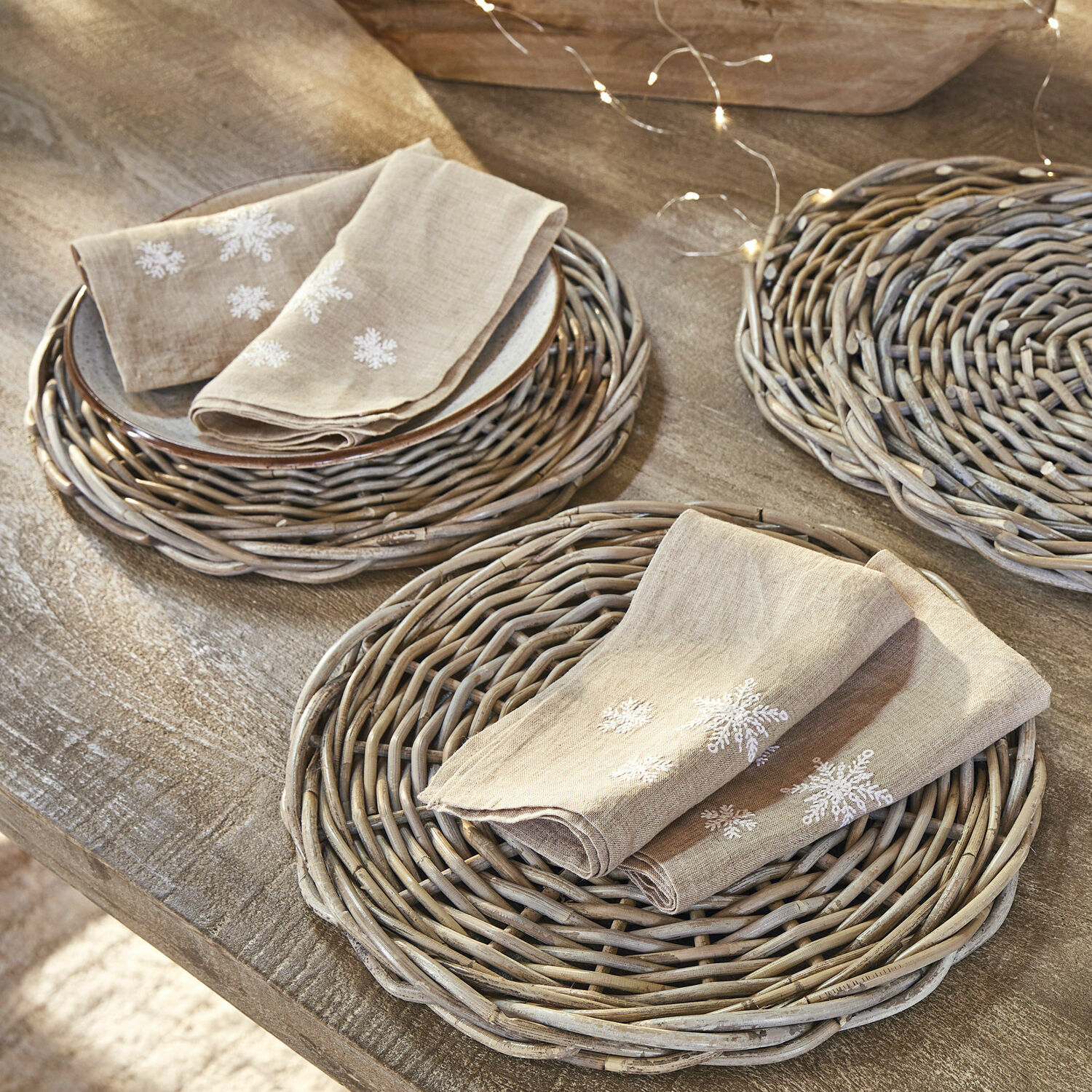Set di 4 tovaglioli Ruspi Tovaglioli in lino beige con ricamo fiocchi di neve su sottopiatti in vimini su tavolo in legno