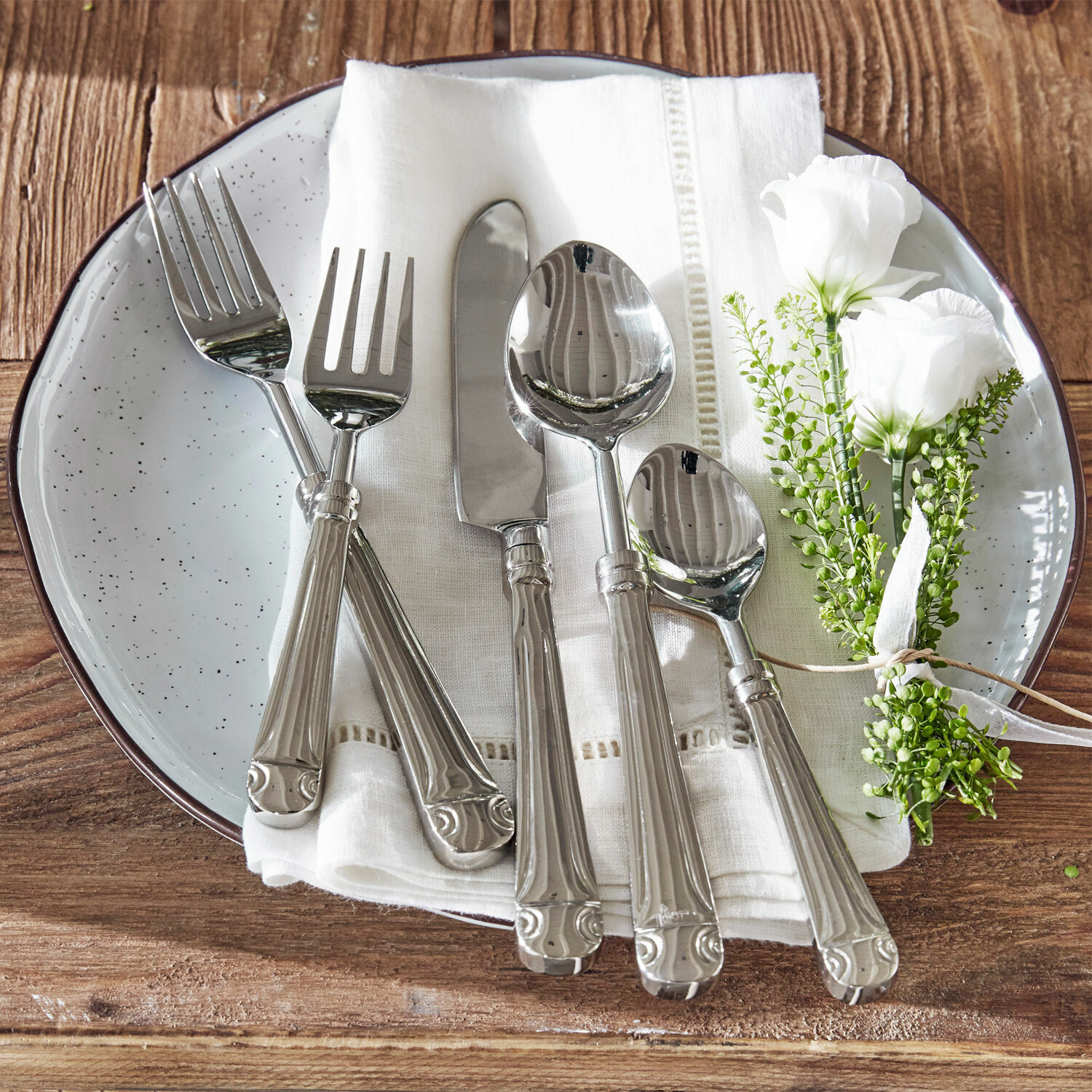 Posate Eriat Set di posate in acciaio su tovagliolo bianco con decorazione floreale su tavolo in legno