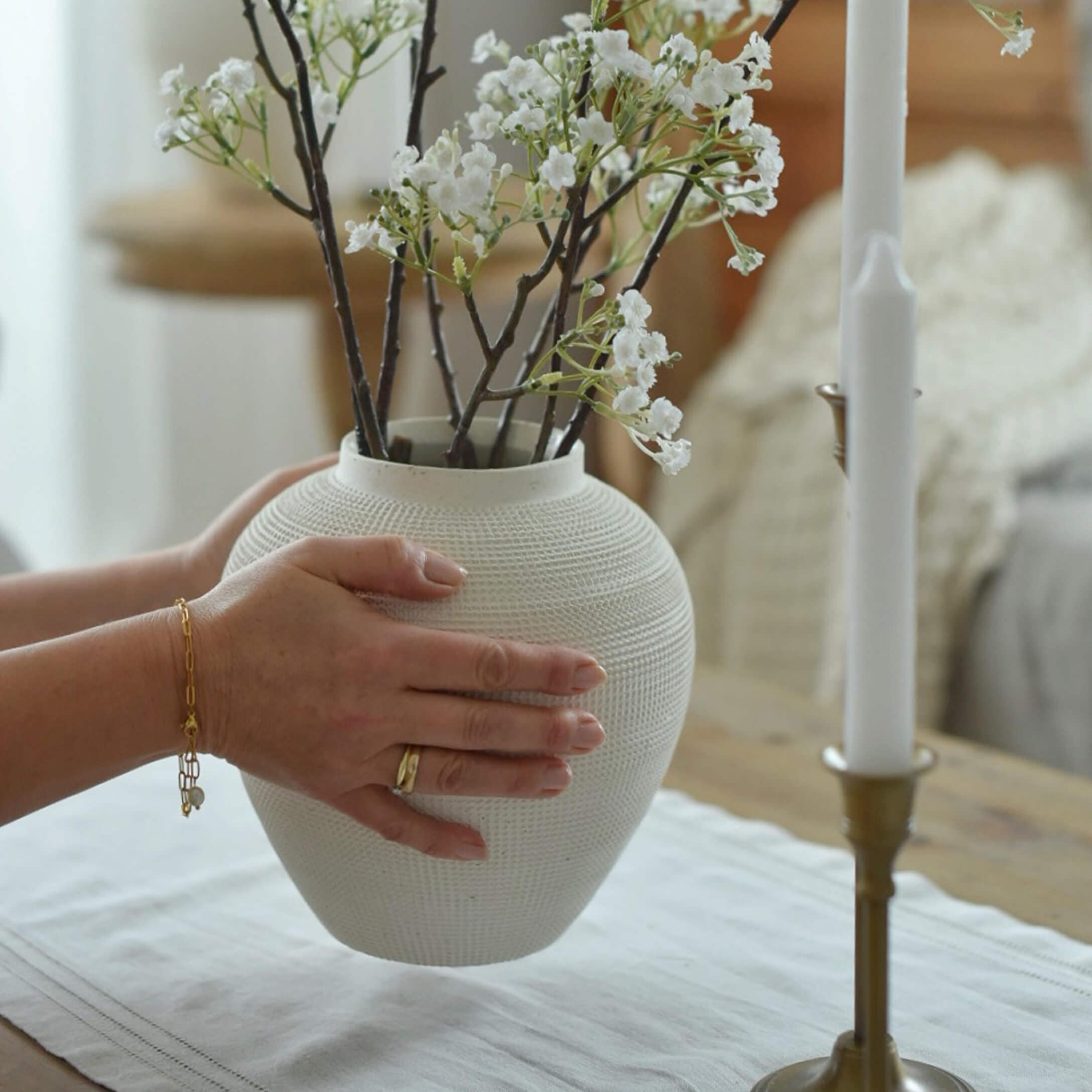 Vaso in ceramica bianca con texture tenuto da mani con rami di fiori bianchi su tavolo