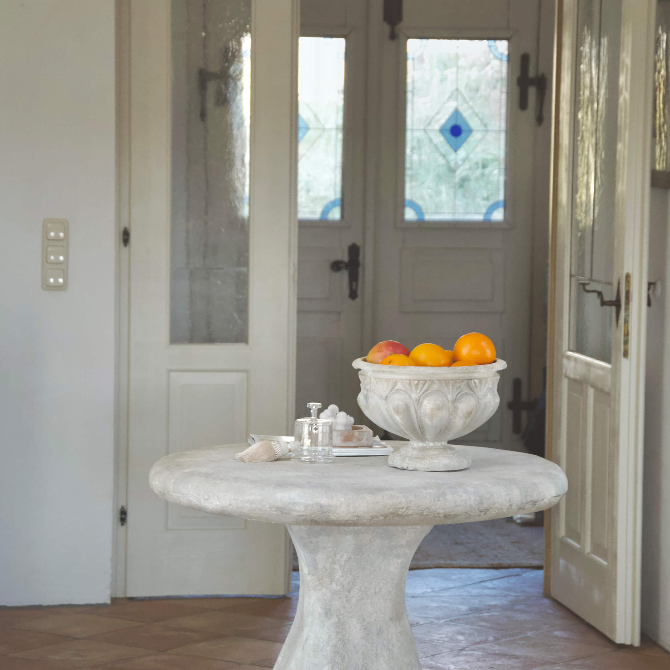 Tavolo rotondo in cemento chiaro con ciotola decorativa vintage piena di frutta arancione