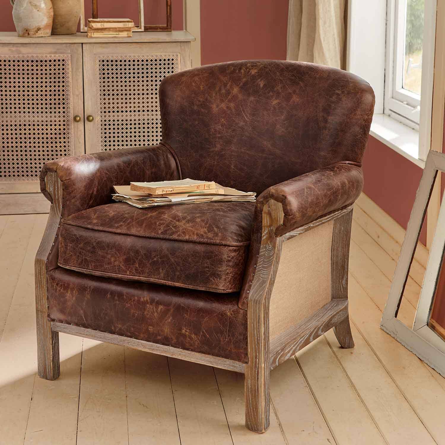 Poltrona marrone in pelle invecchiata con struttura in legno in ambiente rustico con libri