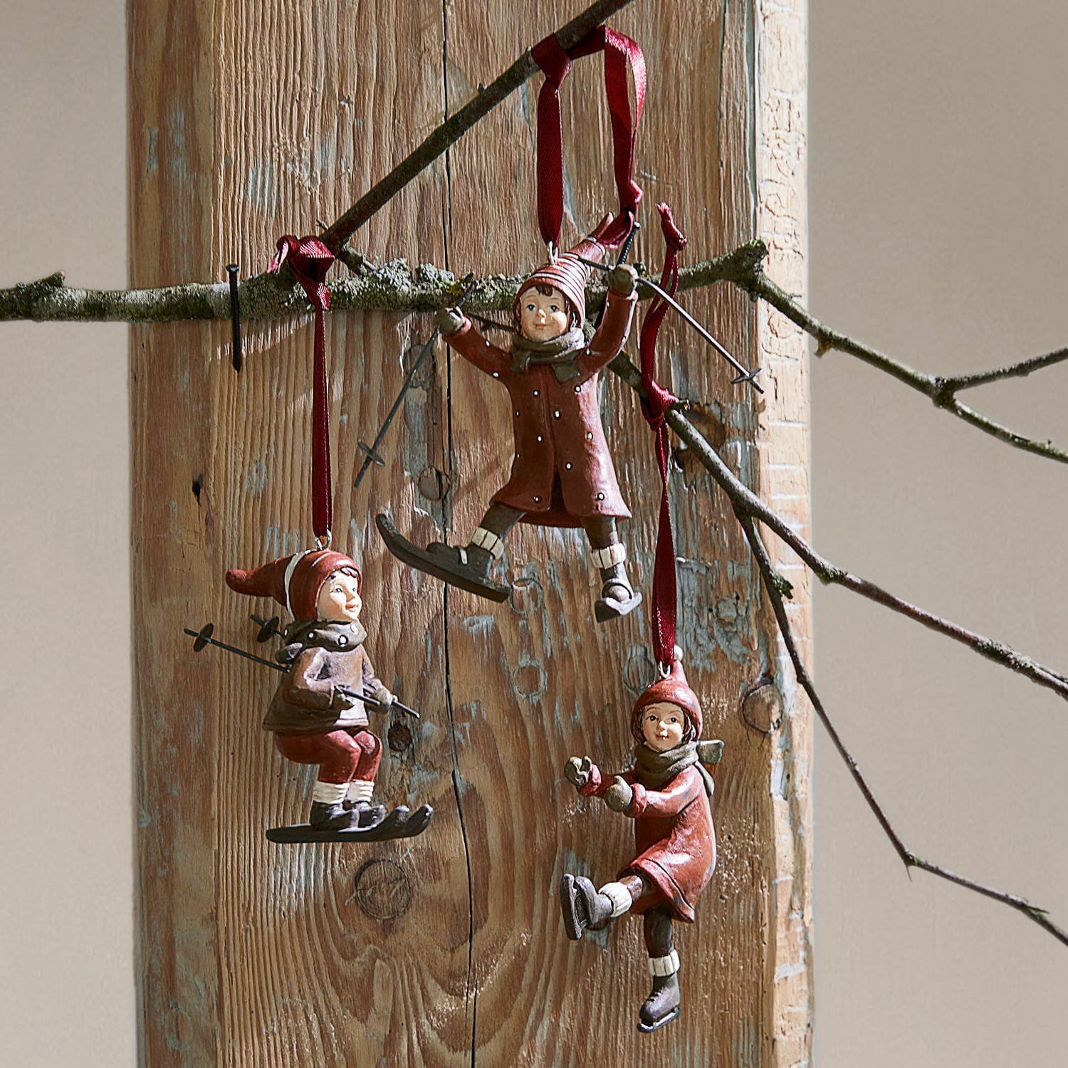 Set di 3 decorazioni da appendere Bibury Tre decorazioni rosse con bambini sugli sci e sul pattinaggio appese su sfondo in legno, decorazione invernale