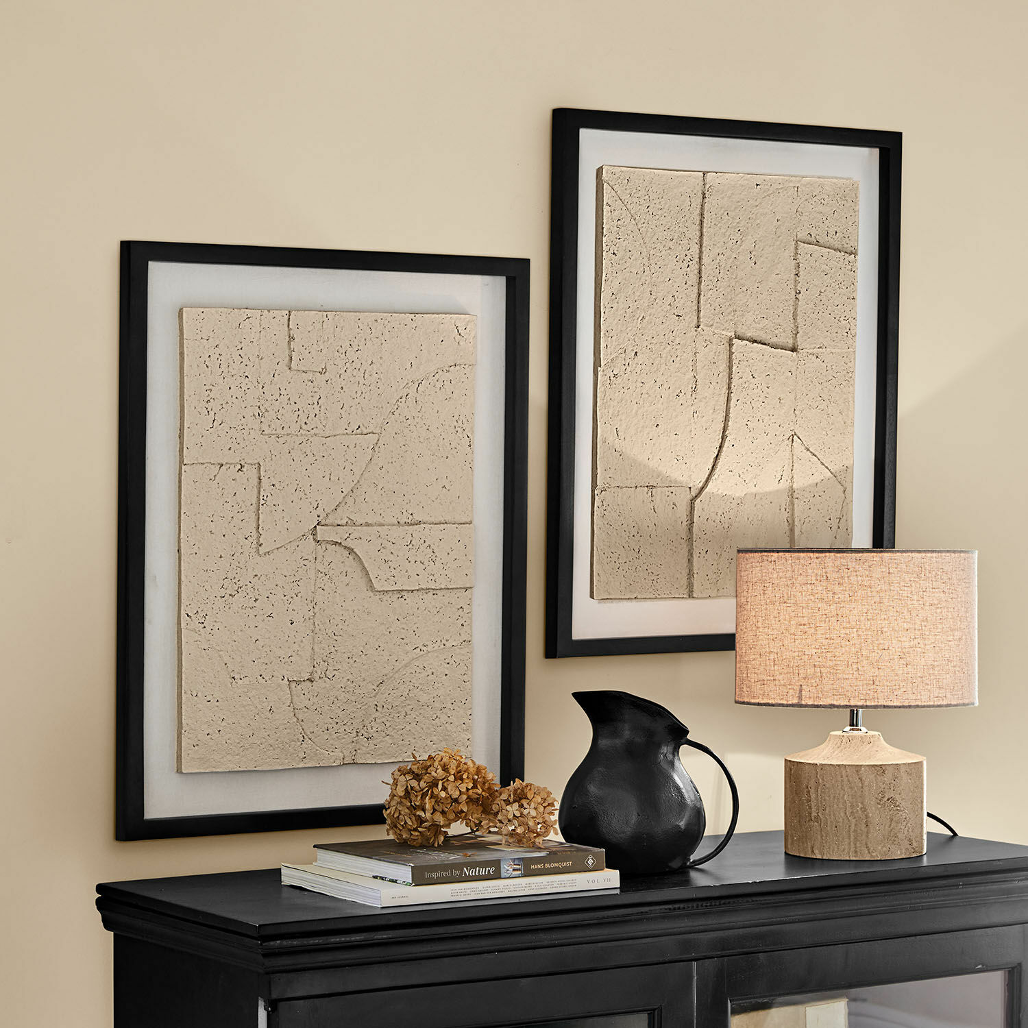 Coppia di quadri Lavinois Due quadri beige in rilievo con cornici nere sopra una credenza nera con lampada e brocca nera