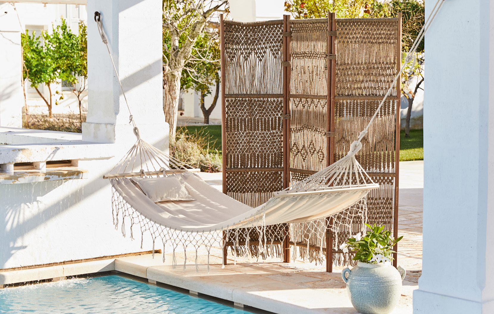 Amaca beige con cuscino e paravento intrecciato su terrazza vicino piscina stile boho