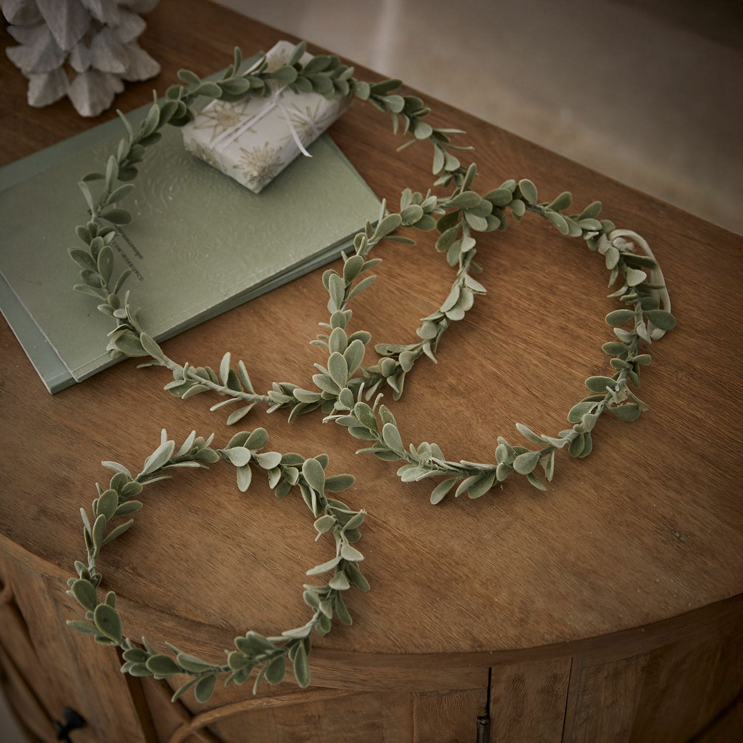 Set di 3 ghirlande Carivela Corone decorative verdi con foglie morbide su tavolo in legno, decorazione naturale per interni