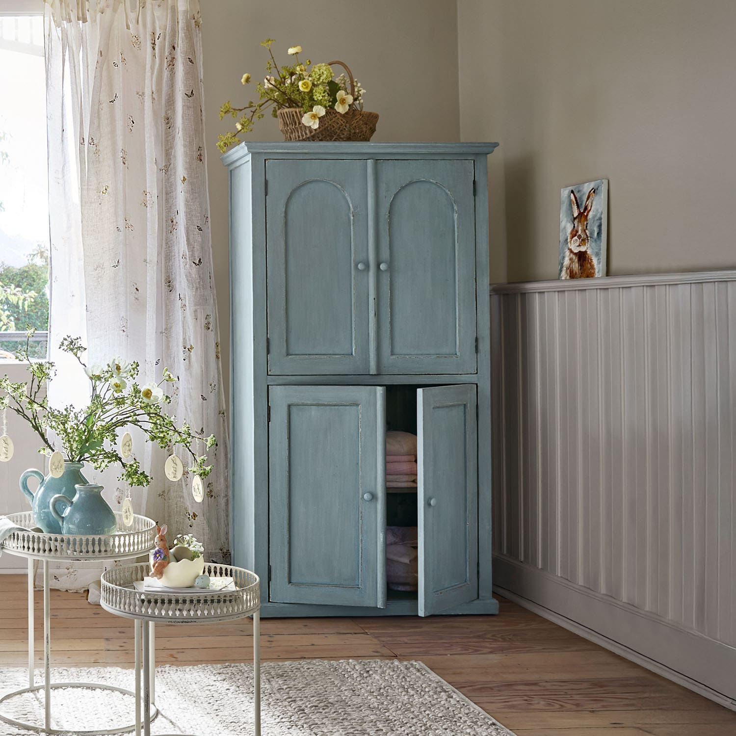 Armadio in legno blu con due coppie di ante in una stanza luminosa e accogliente con decorazioni primaverili