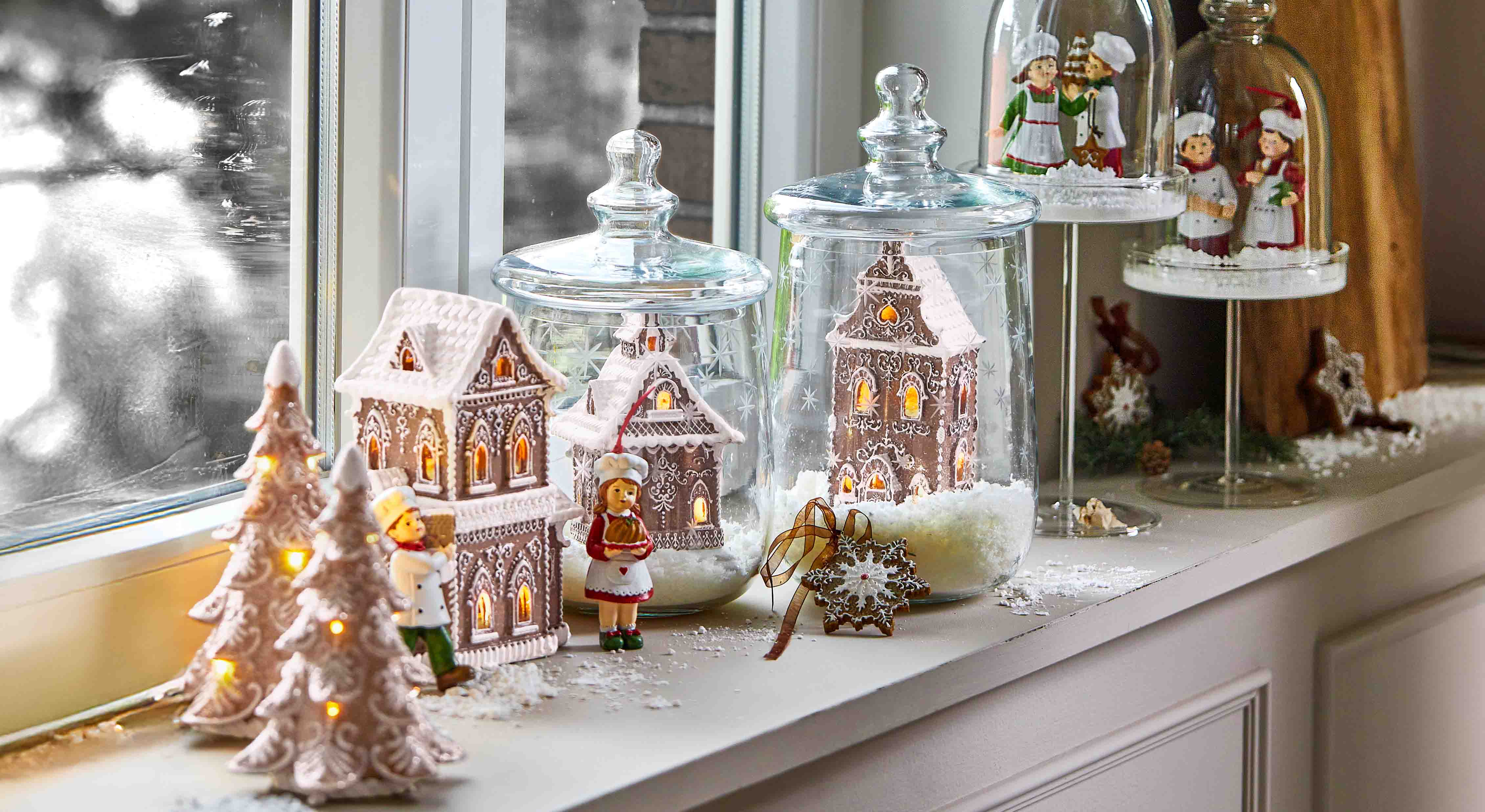 Case di pan di zenzero decorative e figure di cuochi sotto campane di vetro sul davanzale con luci invernali