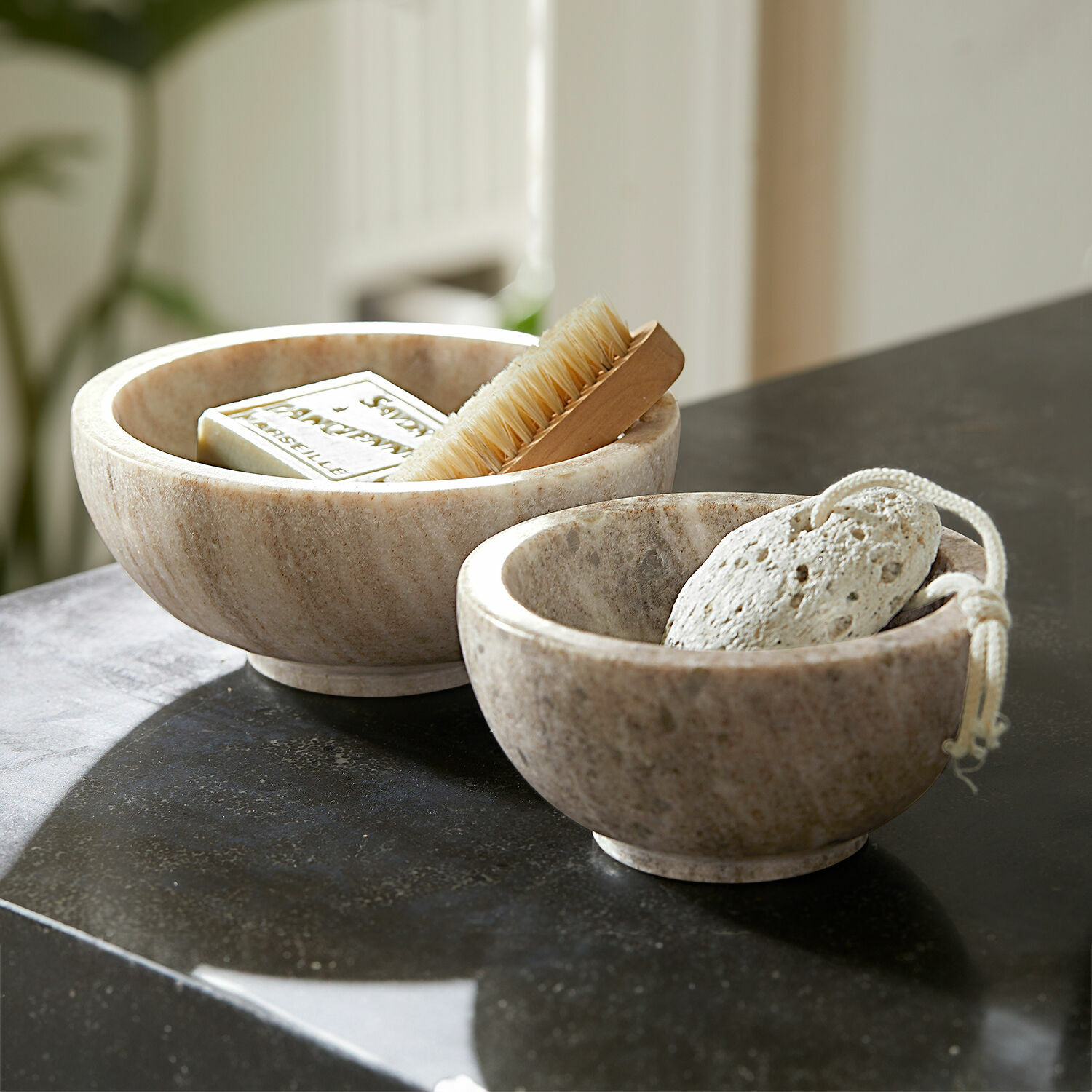 Coppia di ciotole Isamont Due ciotole in marmo colore naturale con sapone, spazzola e pietra pomice su piano bagno nero