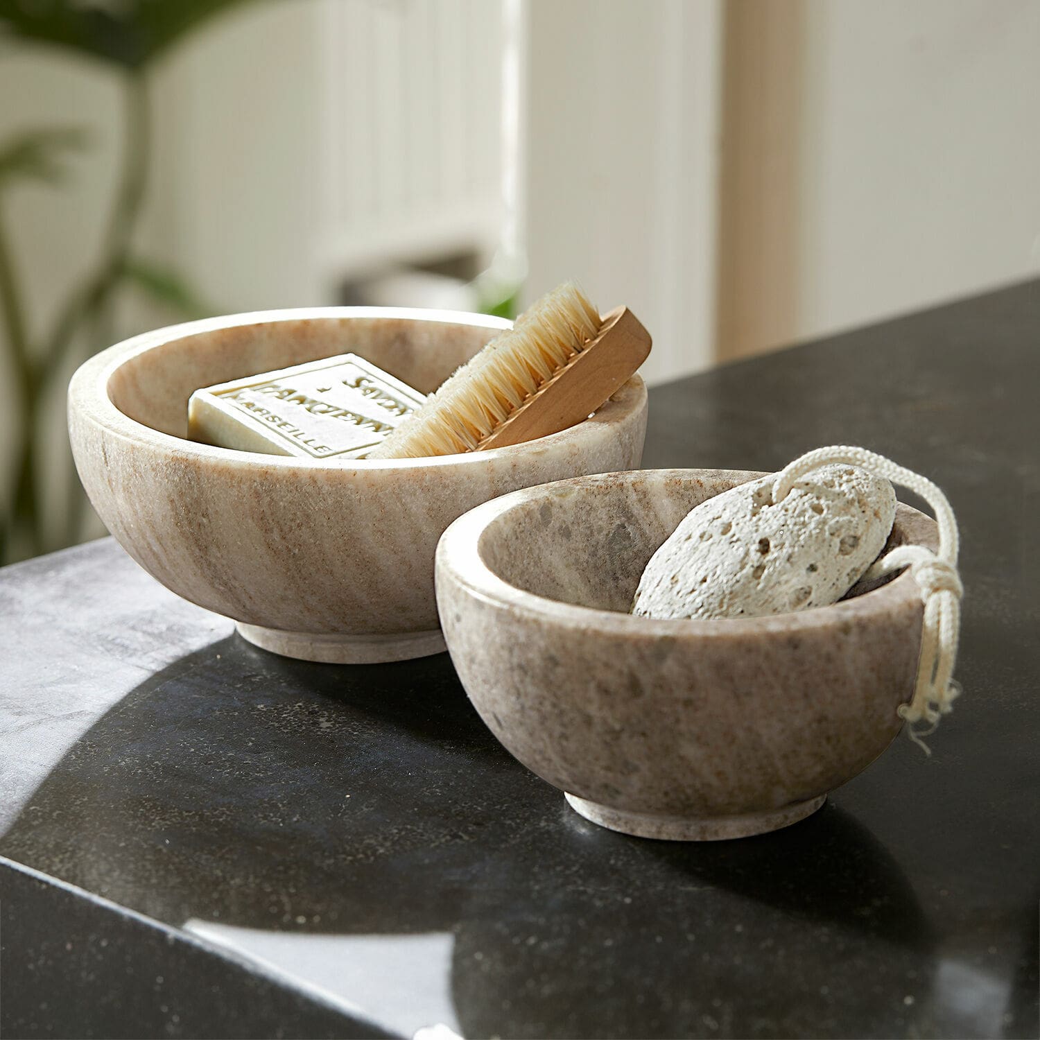 Coppia di ciotole Isamont Due ciotole in marmo colore naturale con sapone, spazzola e pietra pomice su piano bagno nero