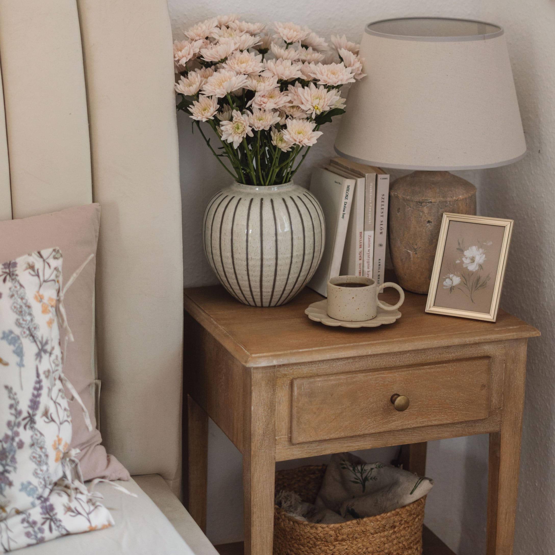 Comodino in legno con lampada in ceramica, vaso con fiori e tazza di caffè in camera accogliente