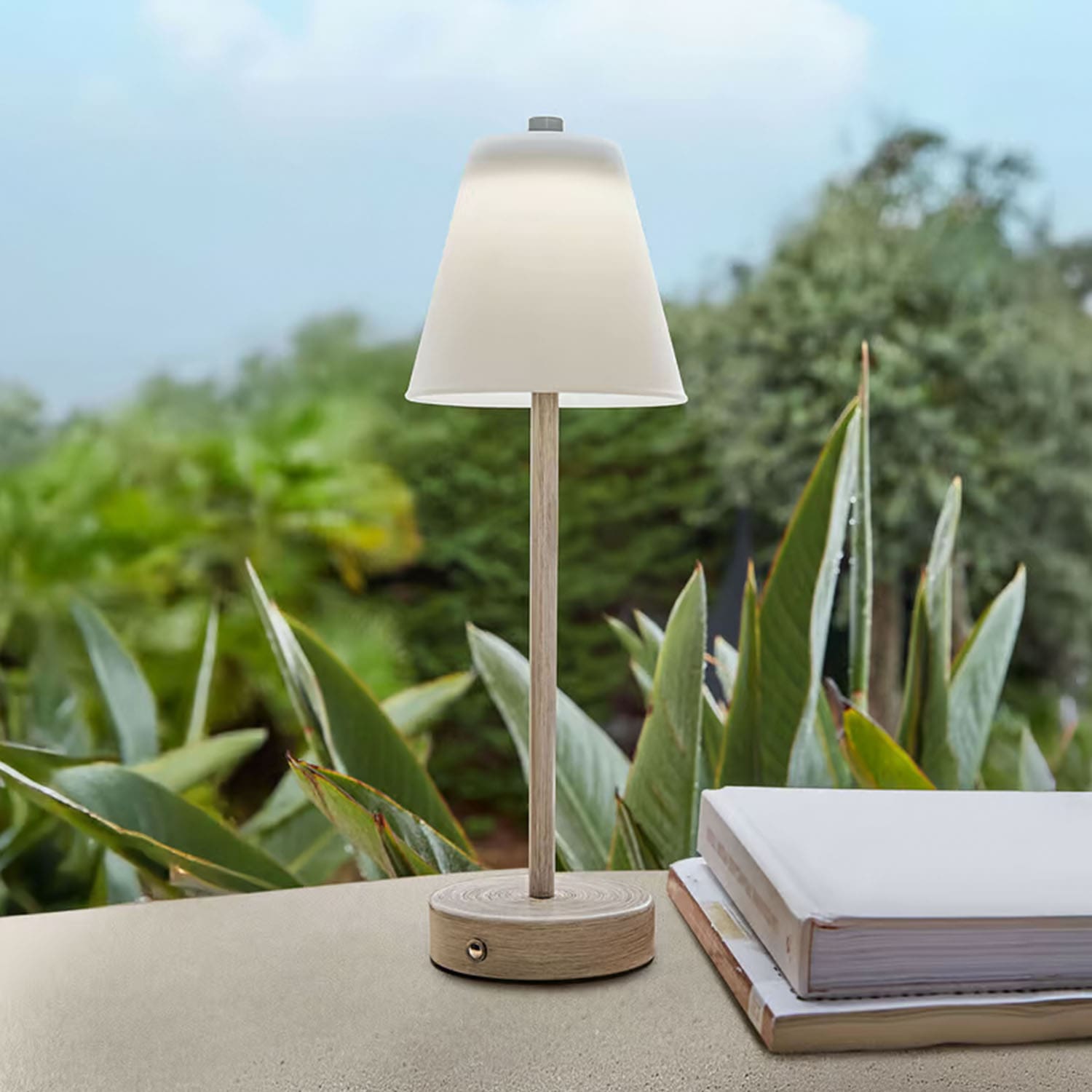 Lampada da tavolo in legno chiaro con paralume bianco davanti a piante verdi, decorazione d'interni