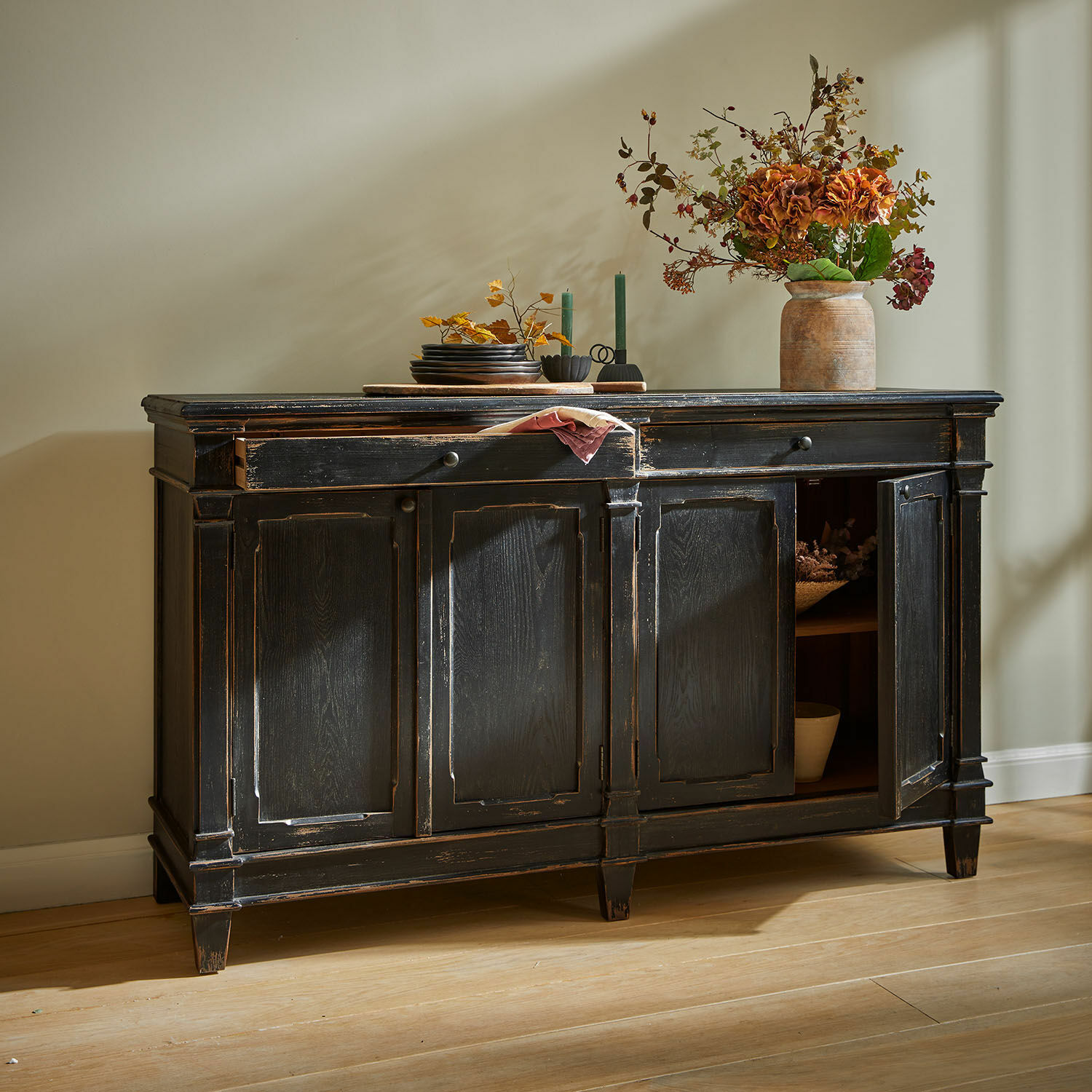 Credenza bassa Chaveline Credenza in legno nero con finitura antica e ante decorative su pavimento in legno chiaro.
