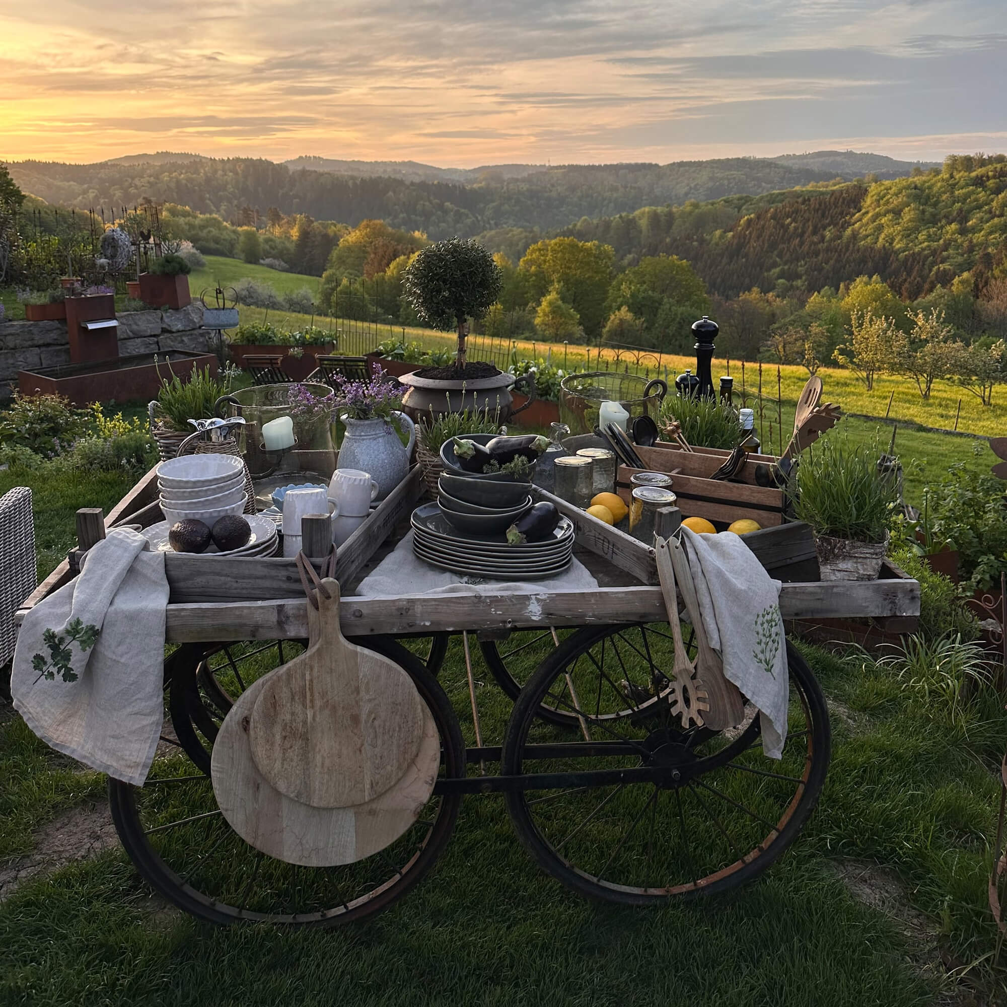 Carretto rustico in legno con stoviglie e decorazioni in giardino verde al tramonto