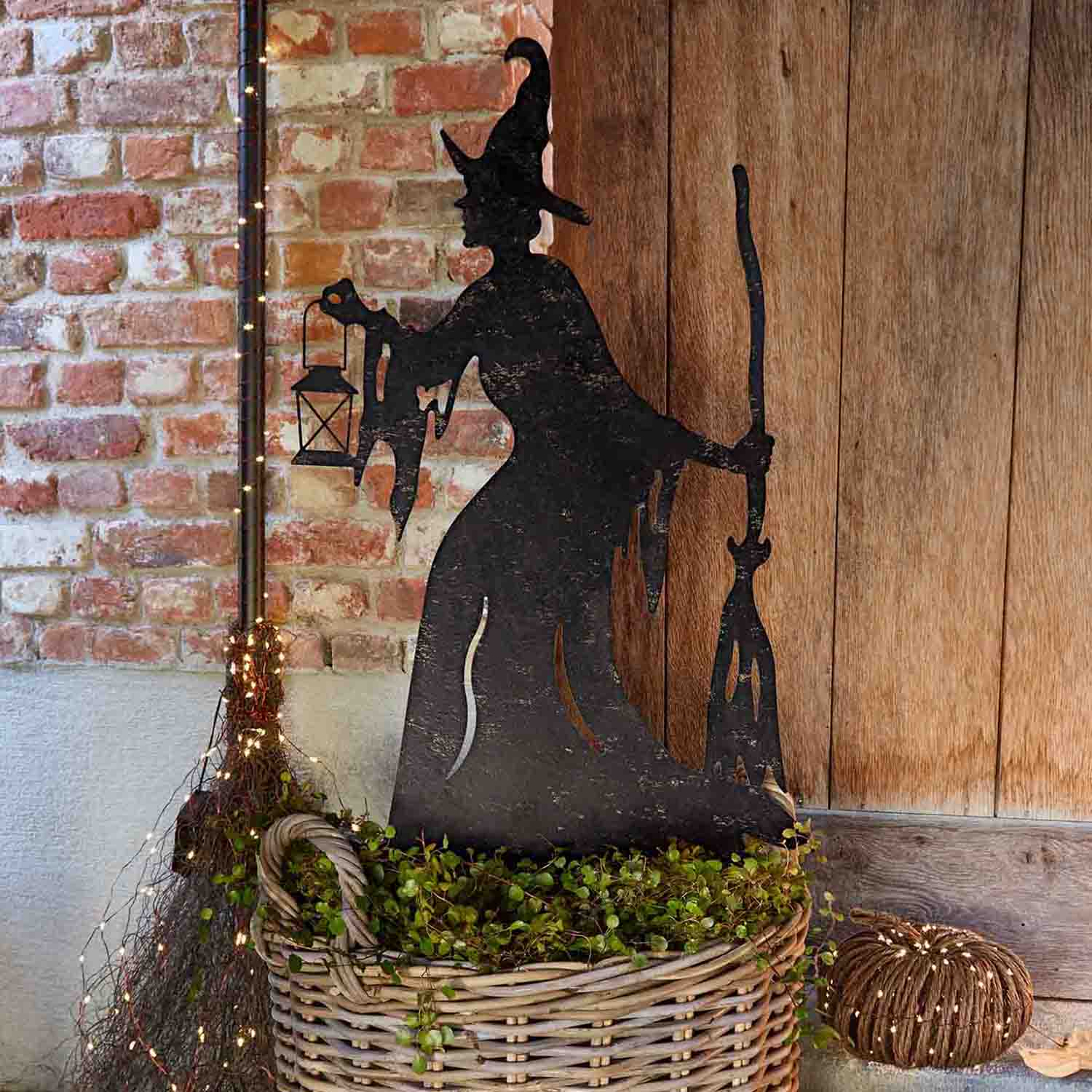 Decorazione in metallo silhouette di strega con lanterna e scopa in cesta di vimini con piante verdi