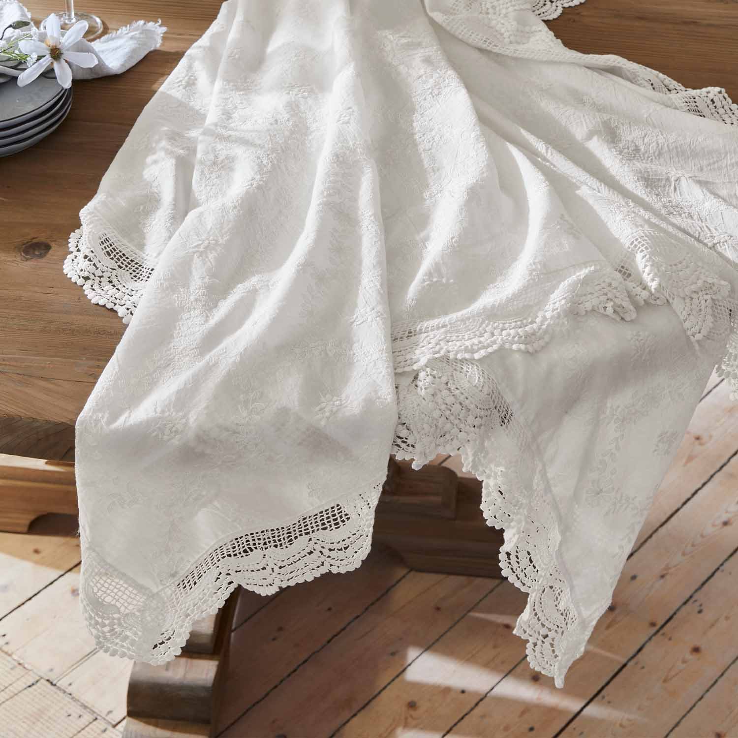 Tovaglia bianca ricamata con bordo in pizzo su tavolo in legno, decorazione elegante per tavola