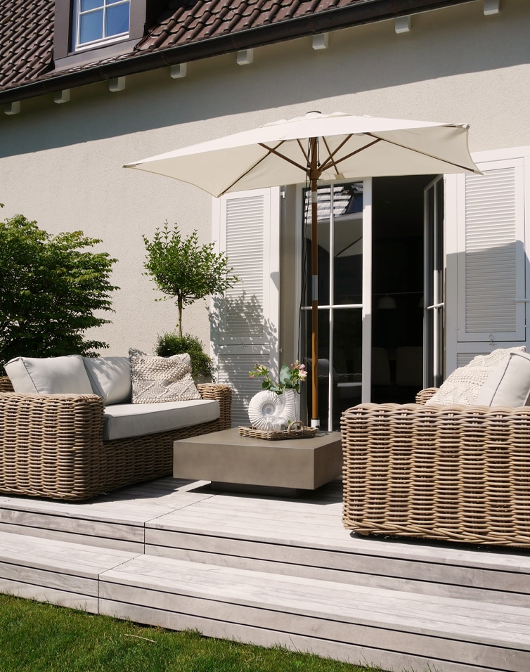 Set moderno di mobili da giardino in rattan beige con ombrellone e cuscini su terrazza in legno chiaro